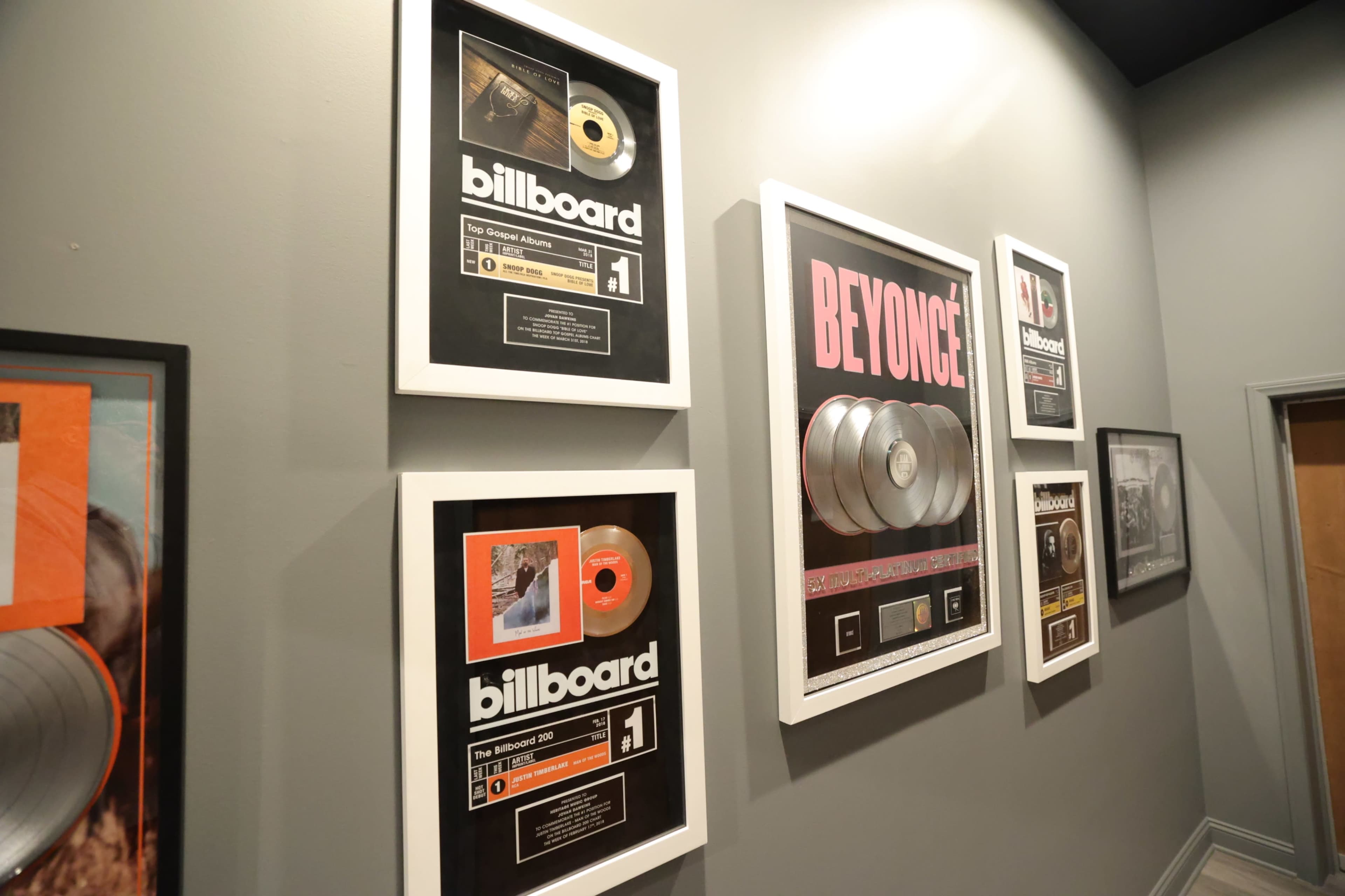 The image shows a wall decorated with framed music awards and records, including Billboard chart accomplishments and a display featuring Beyoncé.