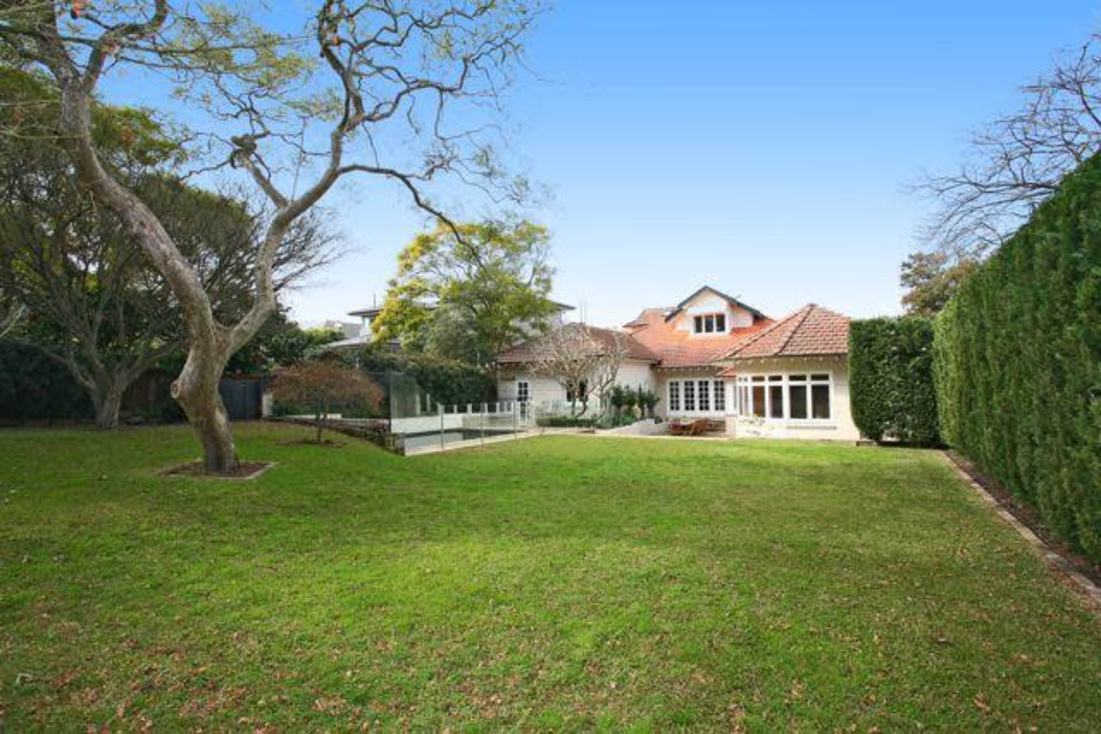 A spacious backyard features a well-maintained lawn with a tree and a house in the background.