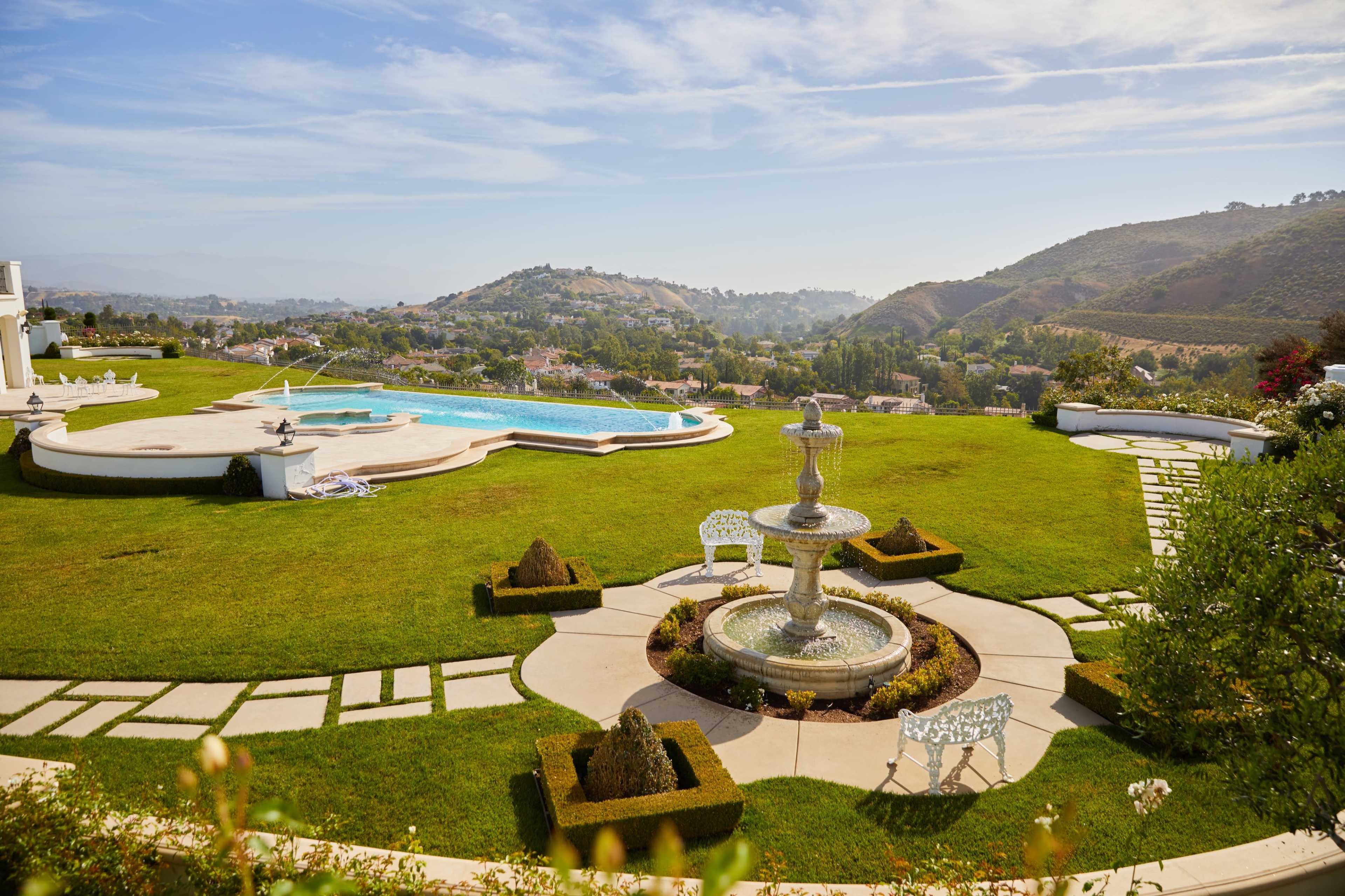 A spacious landscaped area with a swimming pool, fountain, and well-maintained gardens overlooking rolling hills.