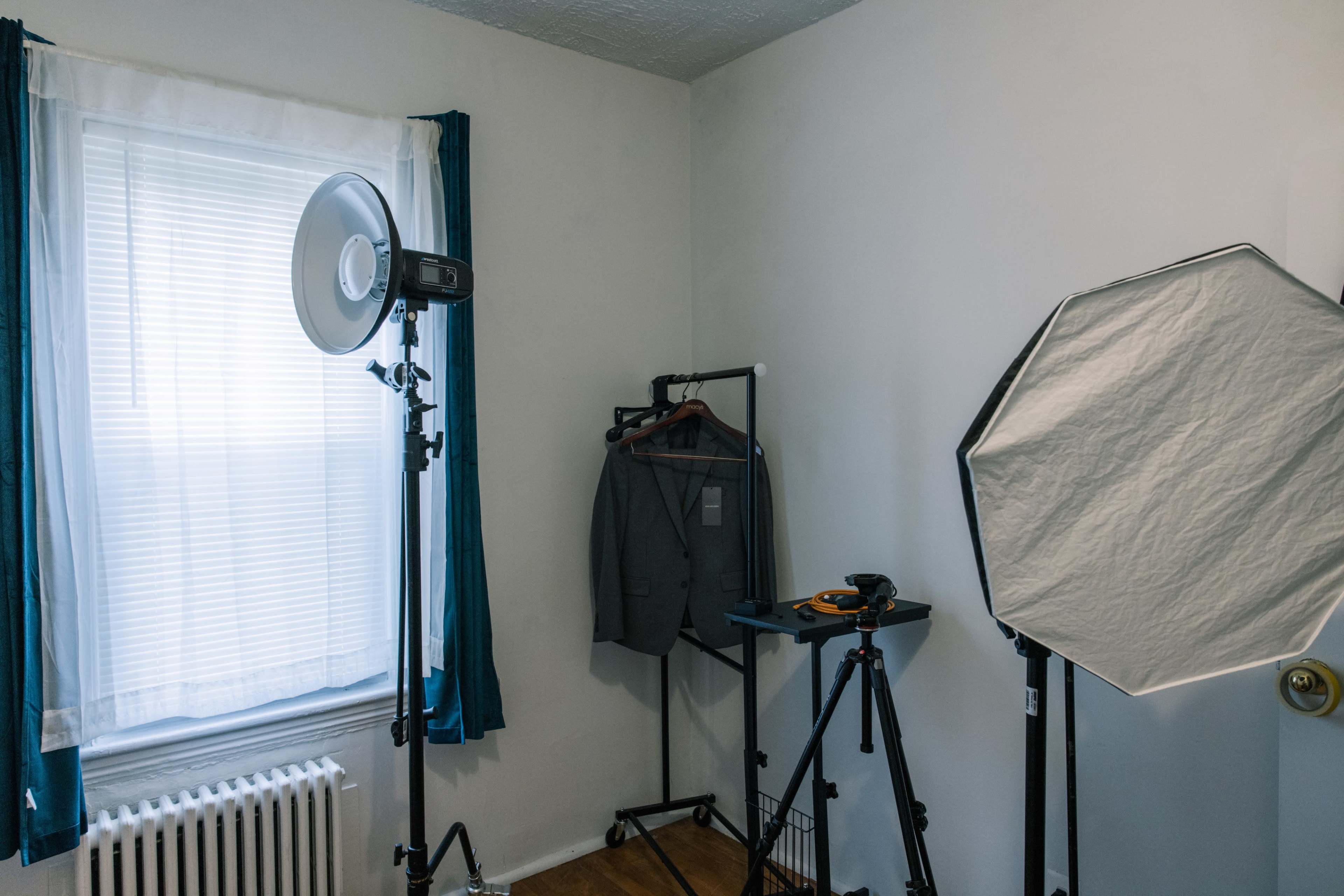 A well-lit room features a suit hanging on a rack next to a ring light and a softbox setup on tripods.