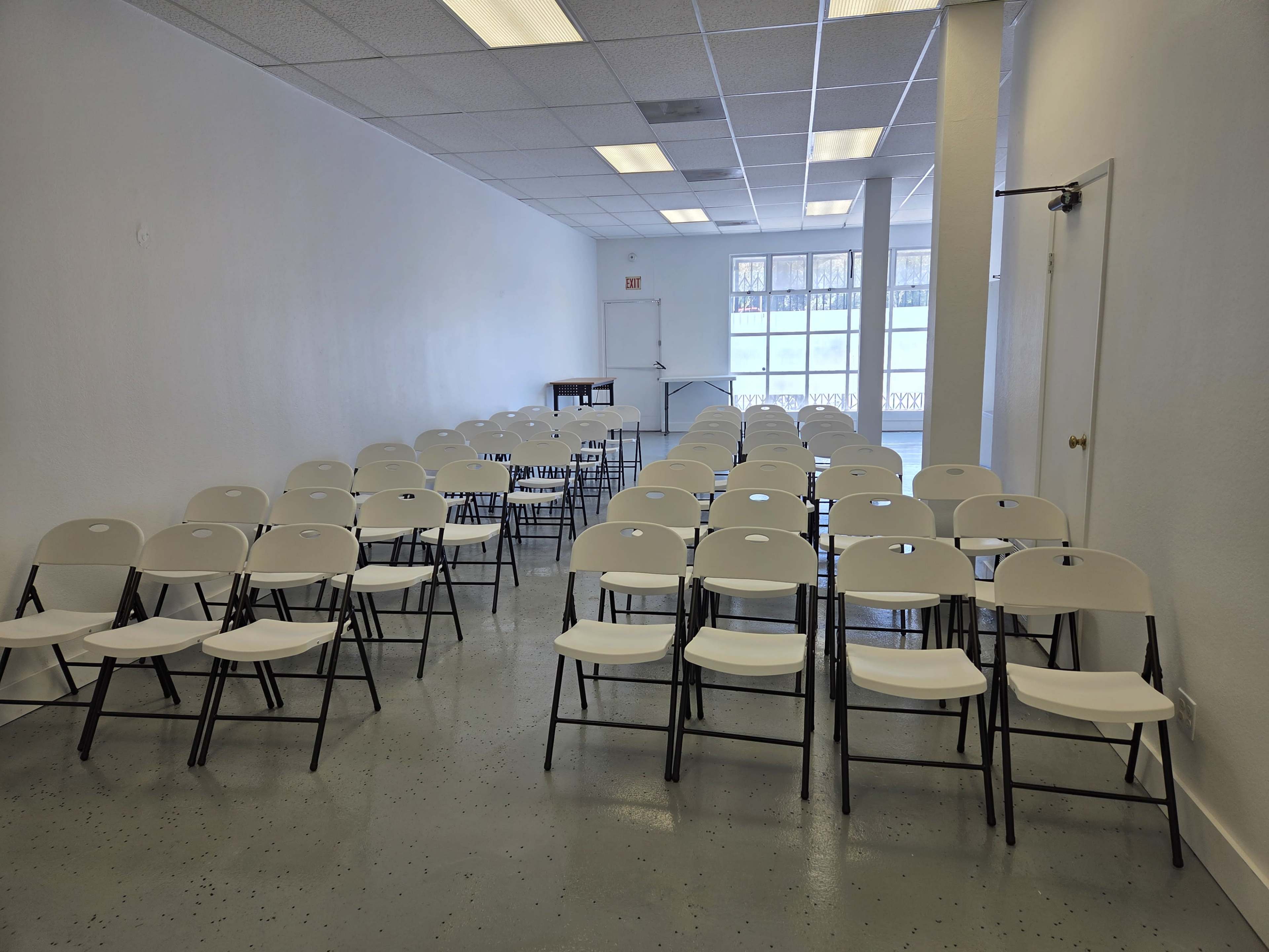 The image shows a spacious interior room with rows of white folding chairs set up for an event.
