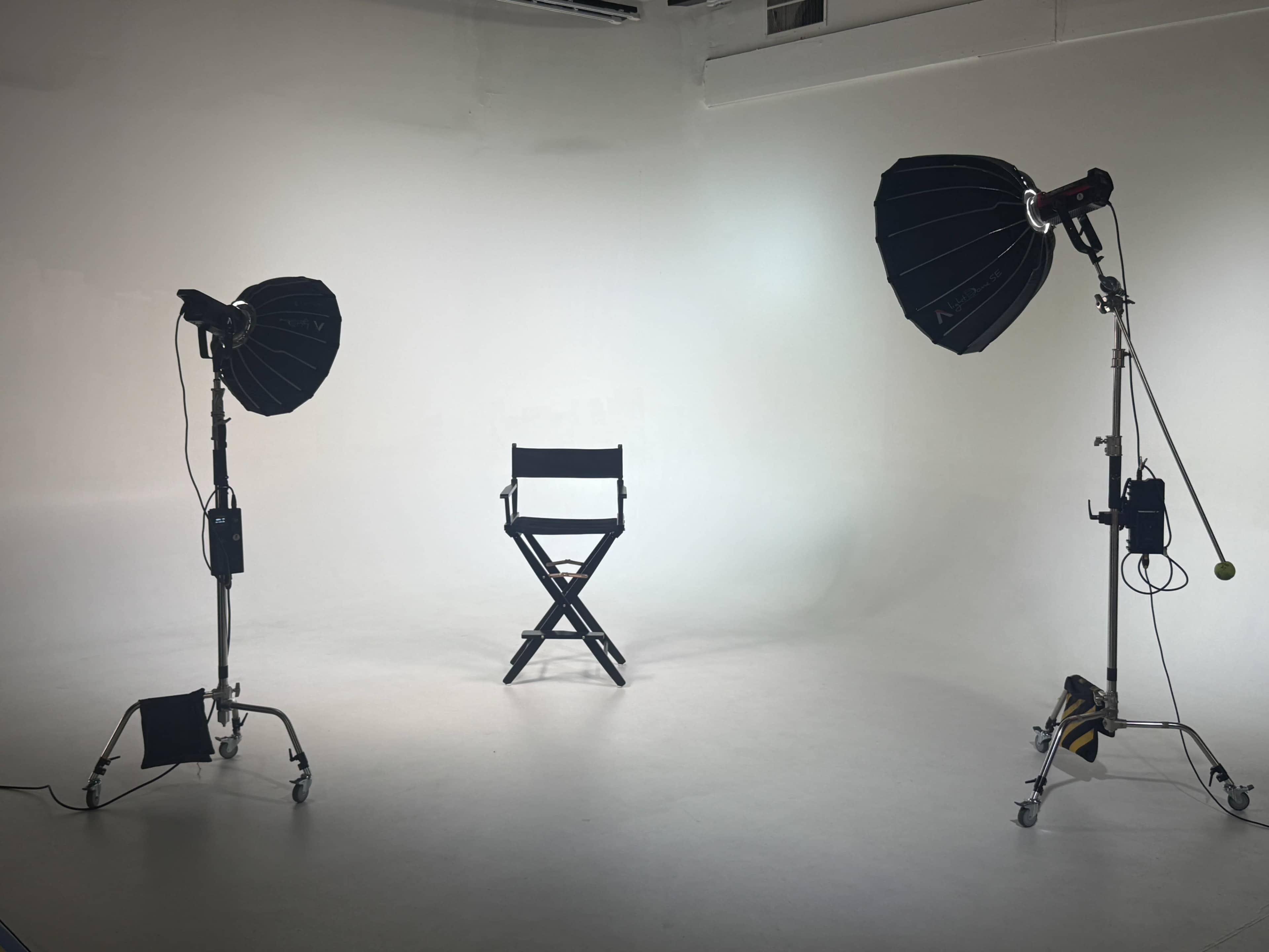 A simple studio setup features a single black director's chair positioned between two softbox lights against a white backdrop.