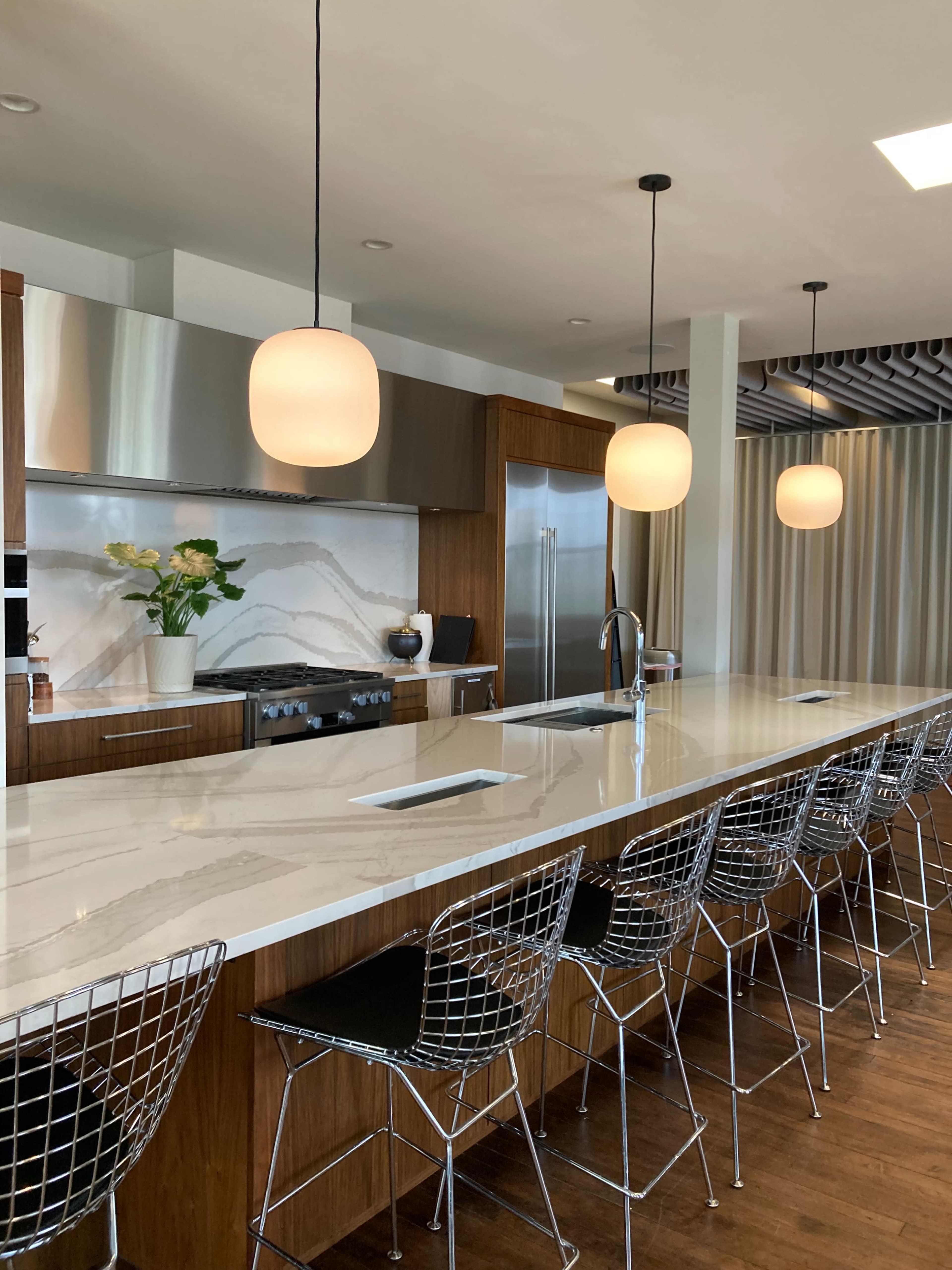 The image shows a modern kitchen with a long island bar featuring wire stools, sleek cabinetry, and pendant lighting above.