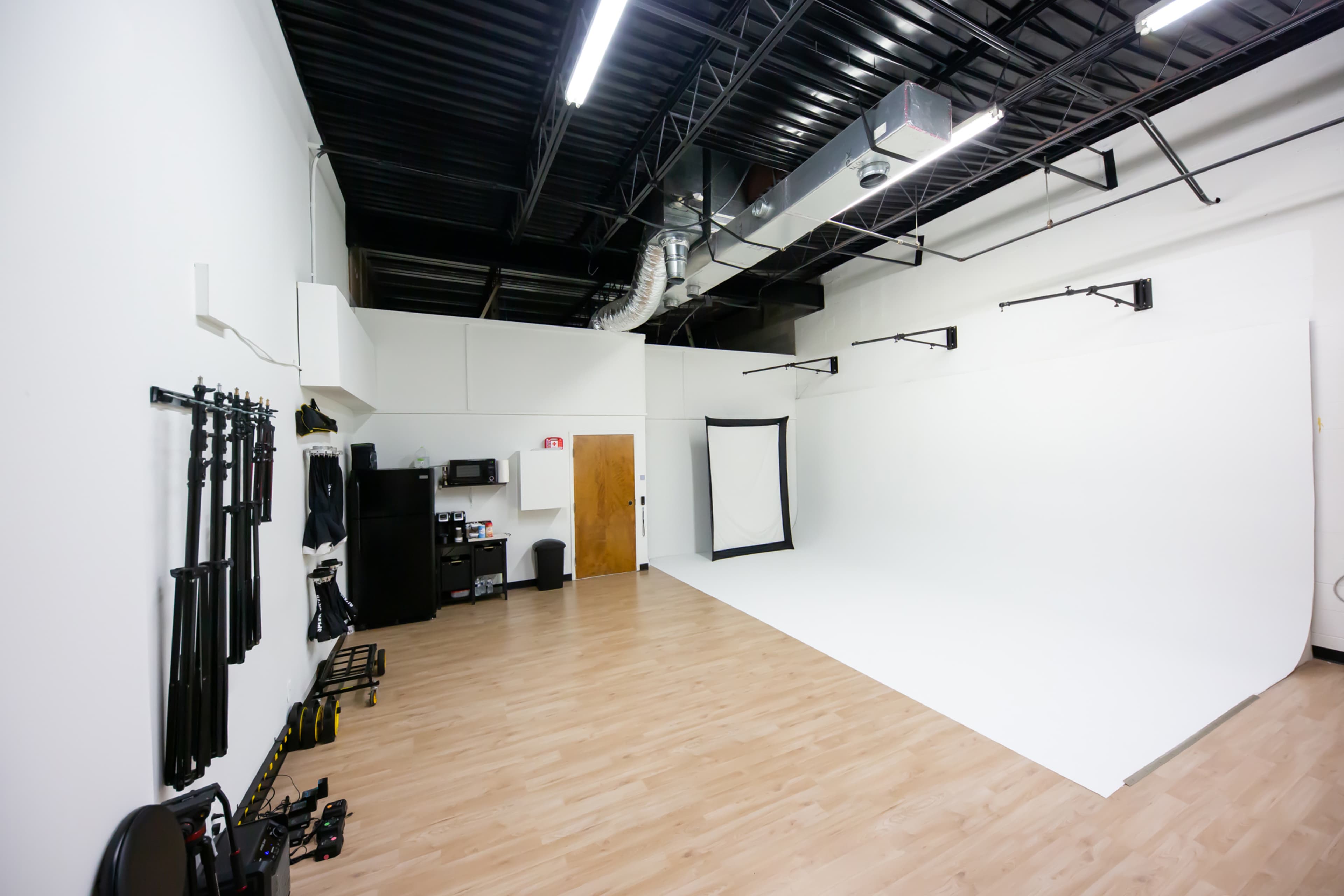 A spacious photography studio with white walls, a hardwood floor, and equipment along one side.