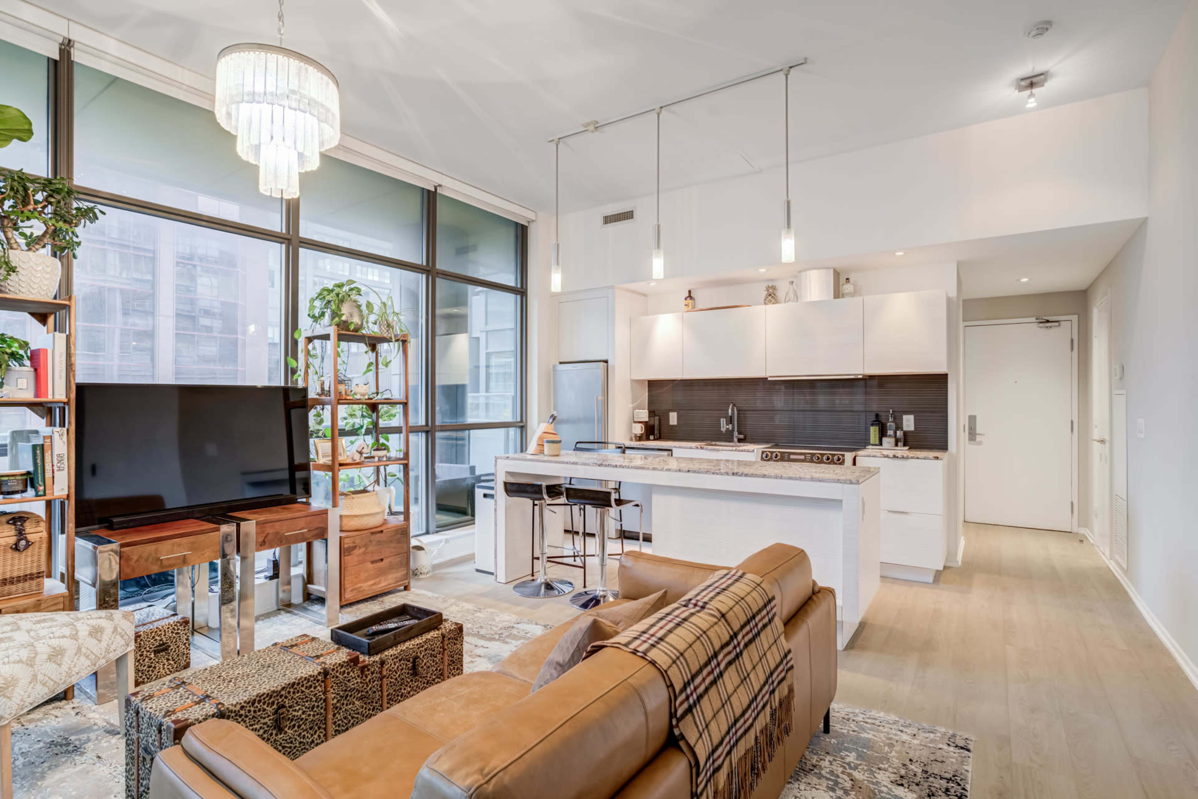The image shows a modern studio apartment with a kitchen, living area, and large windows offering natural light.
