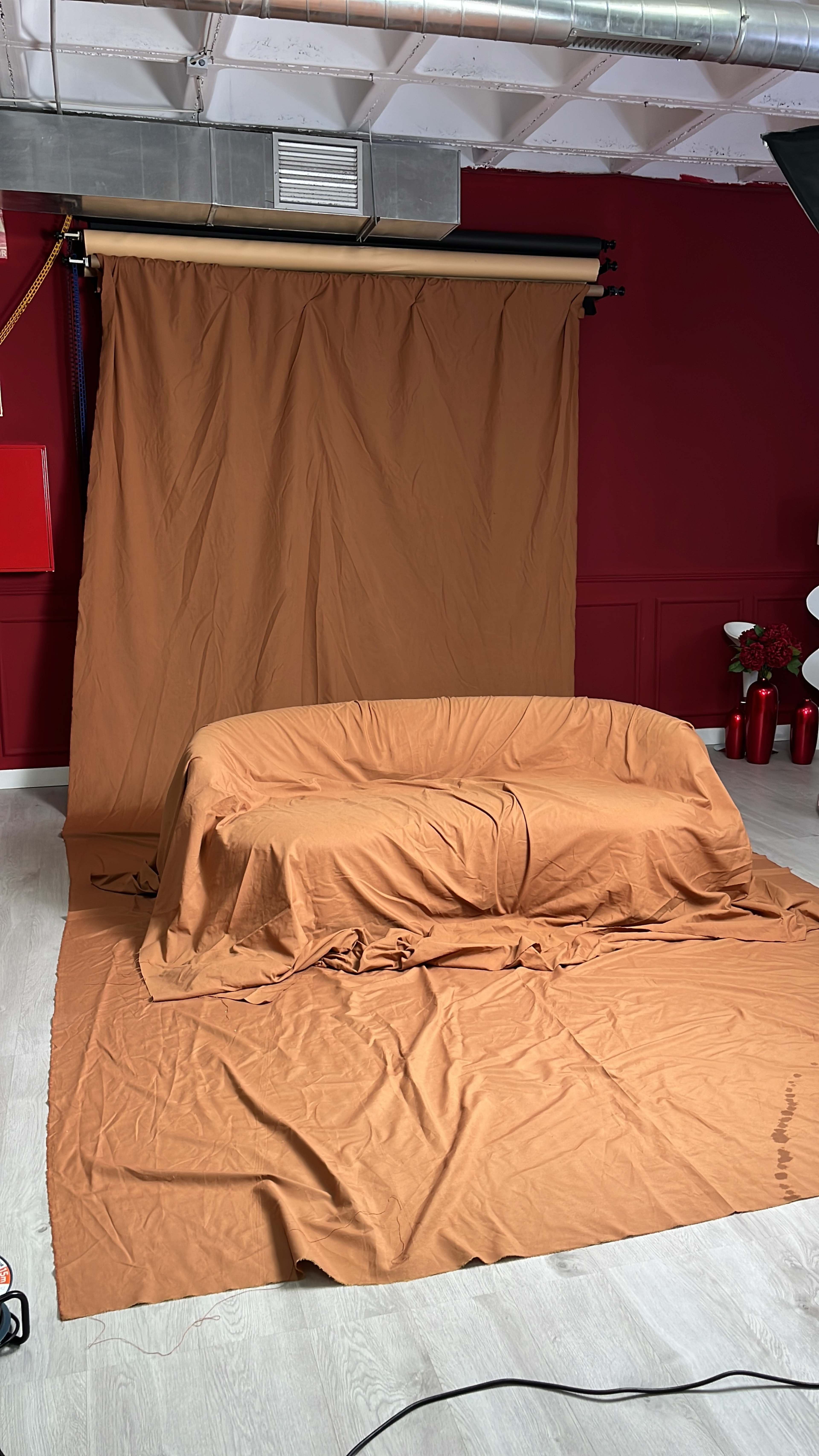 The image shows a photography backdrop setup with a brown fabric draped over a curved sofa and the floor, situated in a studio with a red wall.