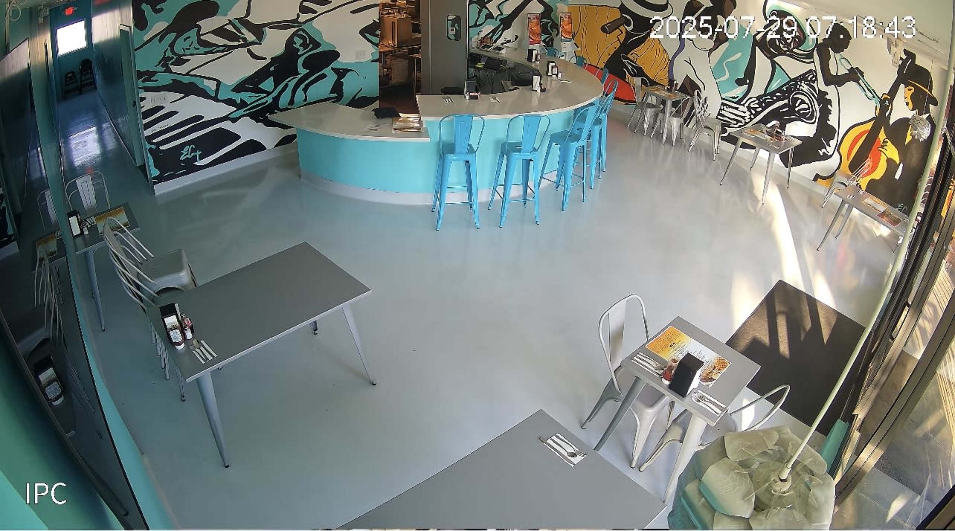 The image shows a brightly colored restaurant interior with turquoise furniture, a bar area, and artistic wall murals featuring dynamic figures.