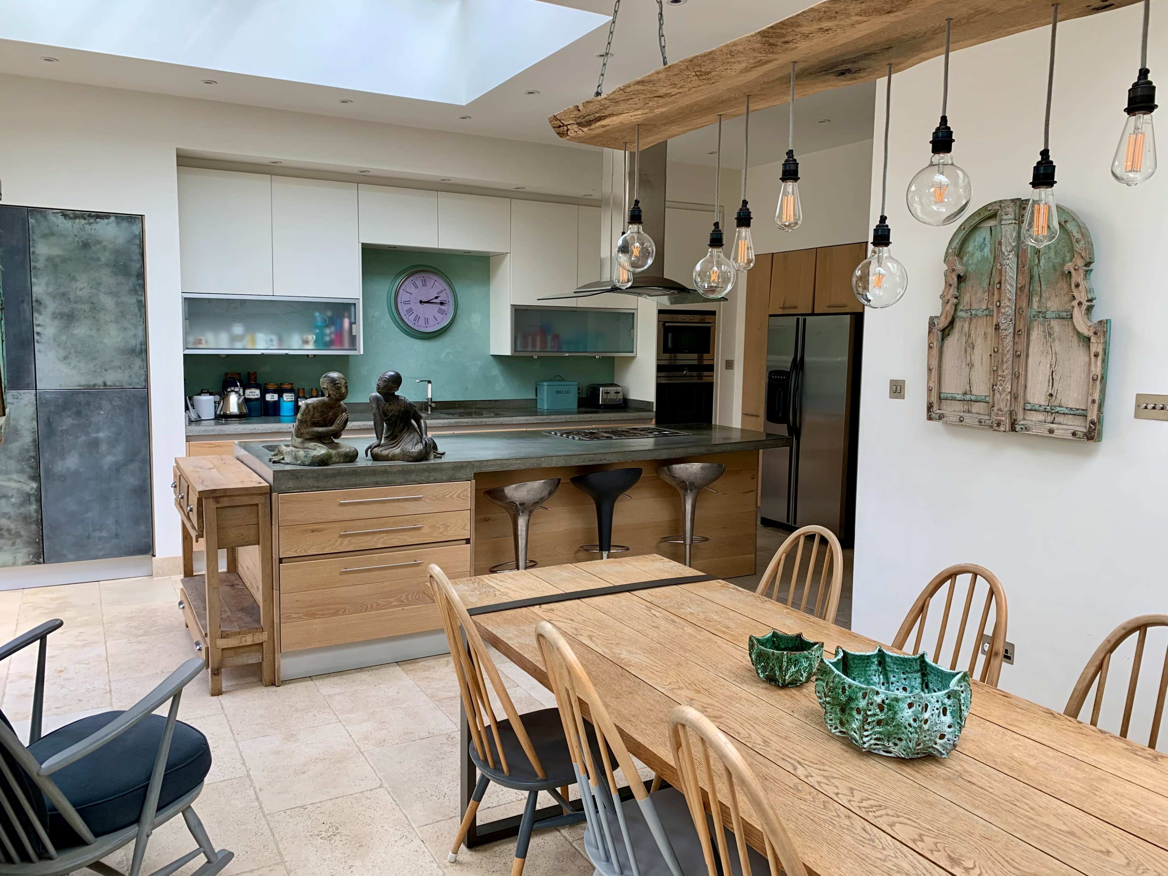 A modern kitchen with a large wooden dining table, stools at a kitchen island, and decorative elements including statues and unique light fixtures.