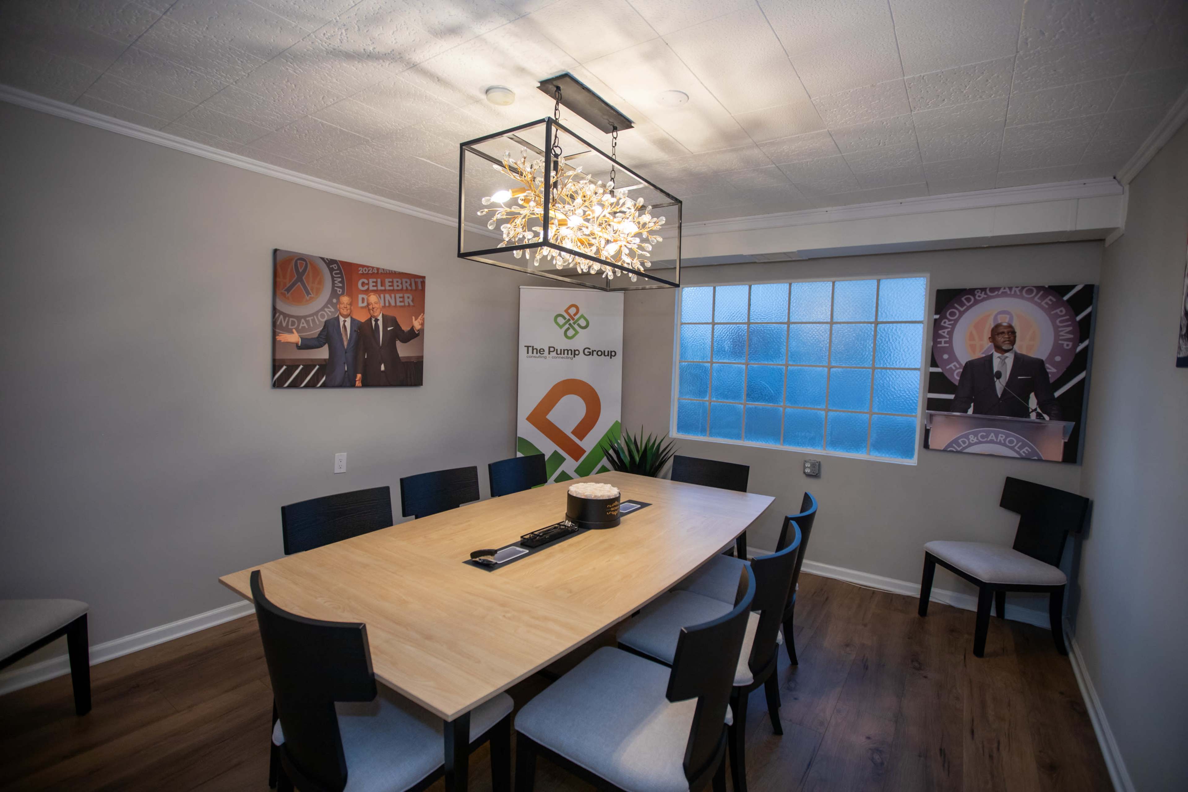 The image shows a conference room with a long wooden table, black chairs, and decorative light fixtures, featuring wall art and branding for The Purge Group.