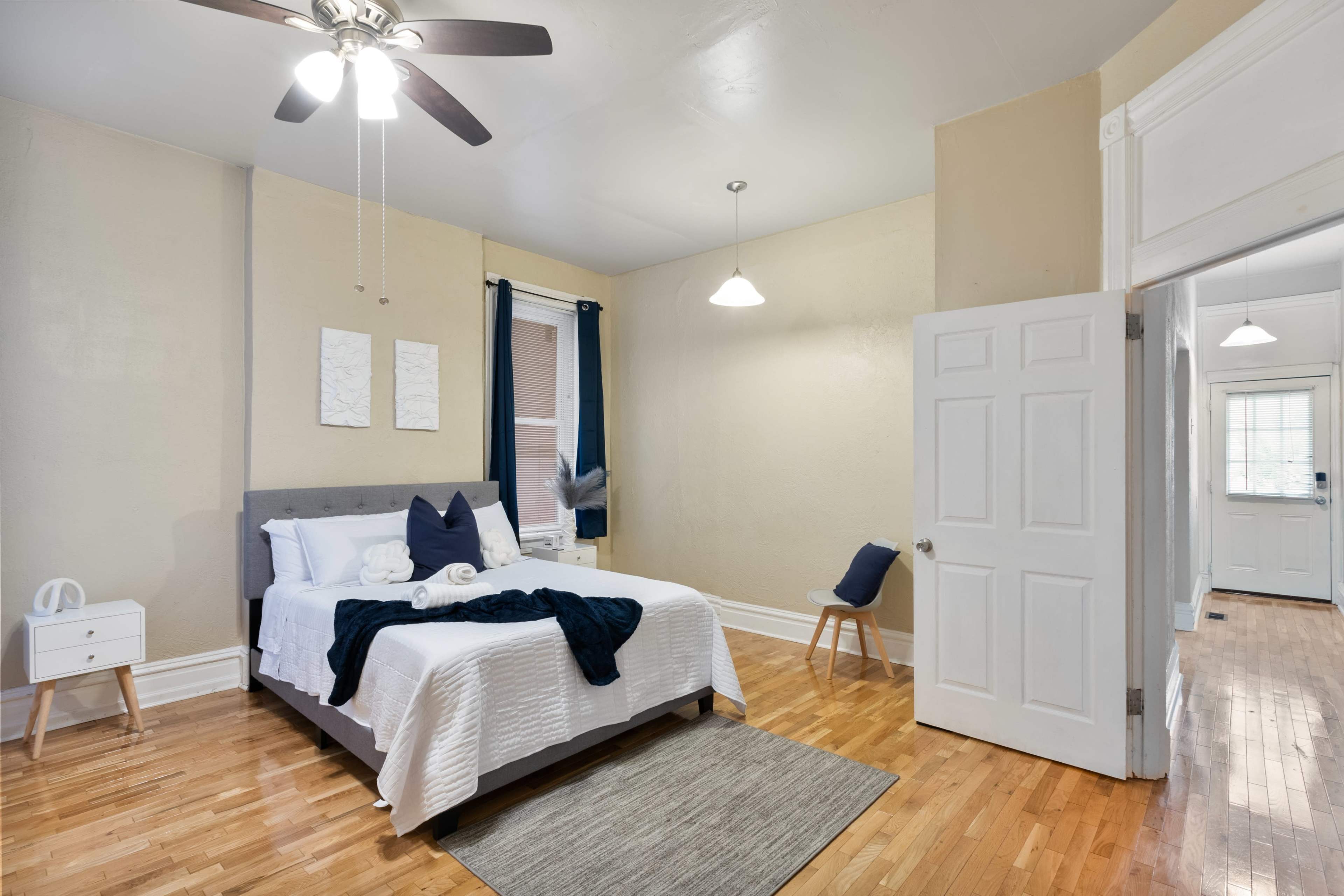 A neatly arranged bedroom with a queen-sized bed, a nightstand, and a door leading to another room.
