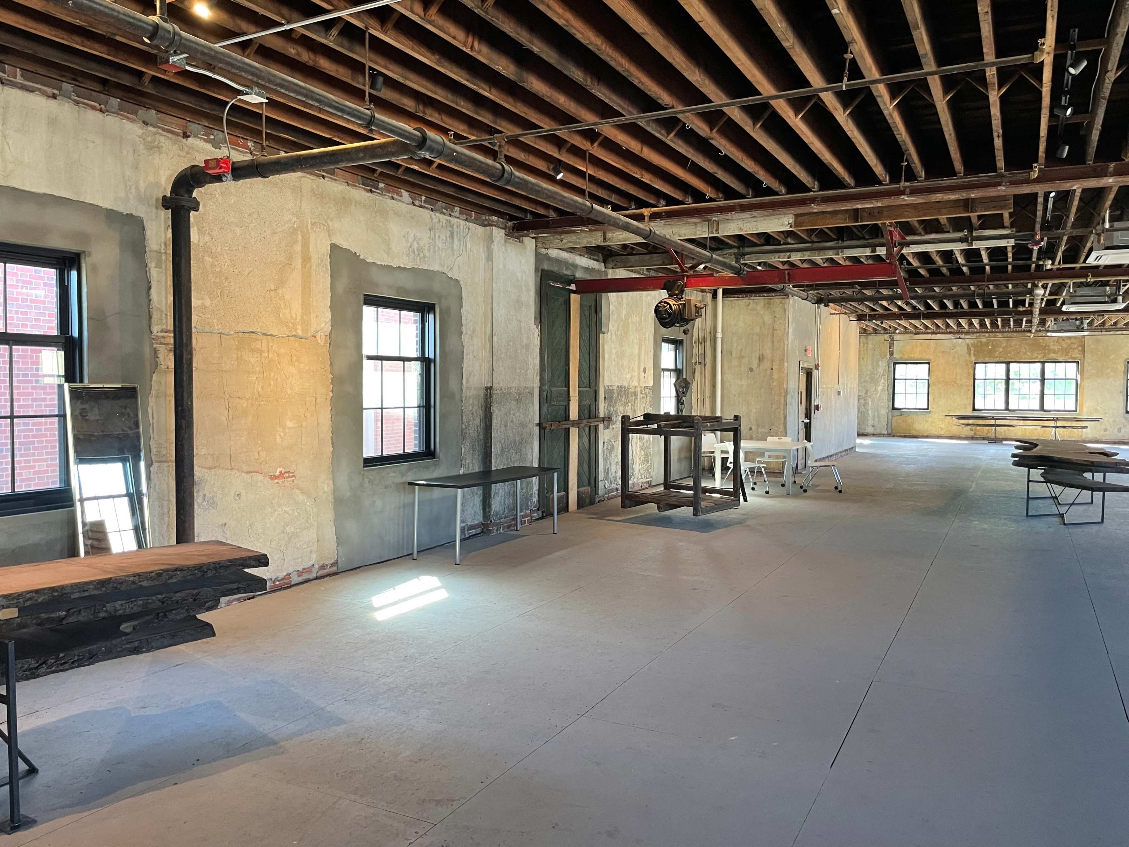 A partially finished interior space featuring exposed beams, unfinished walls, and several wooden tables scattered throughout.