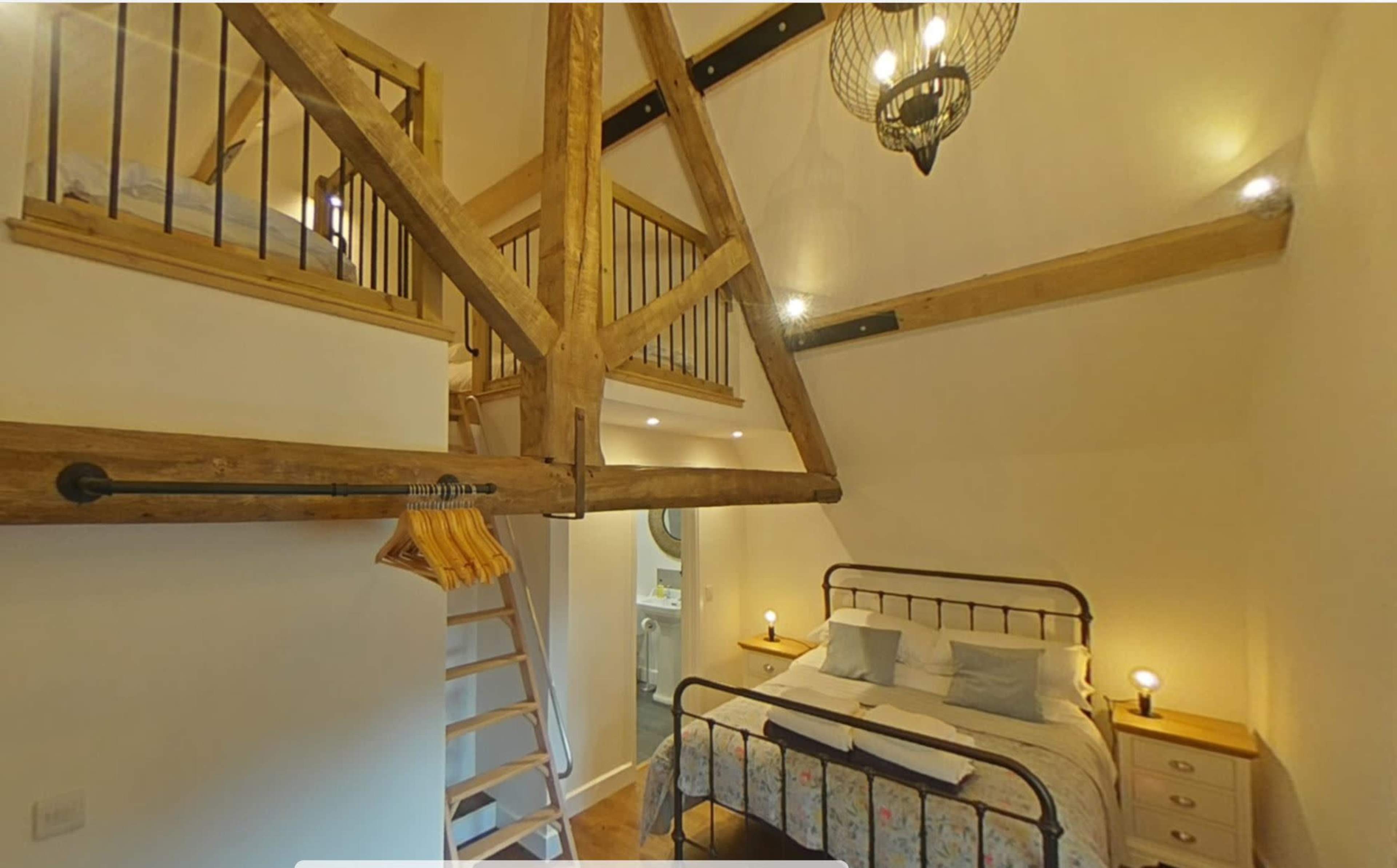 A cozy room with a lofted sleeping area, exposed wooden beams, and a double bed along with a bedside table and a ladder.