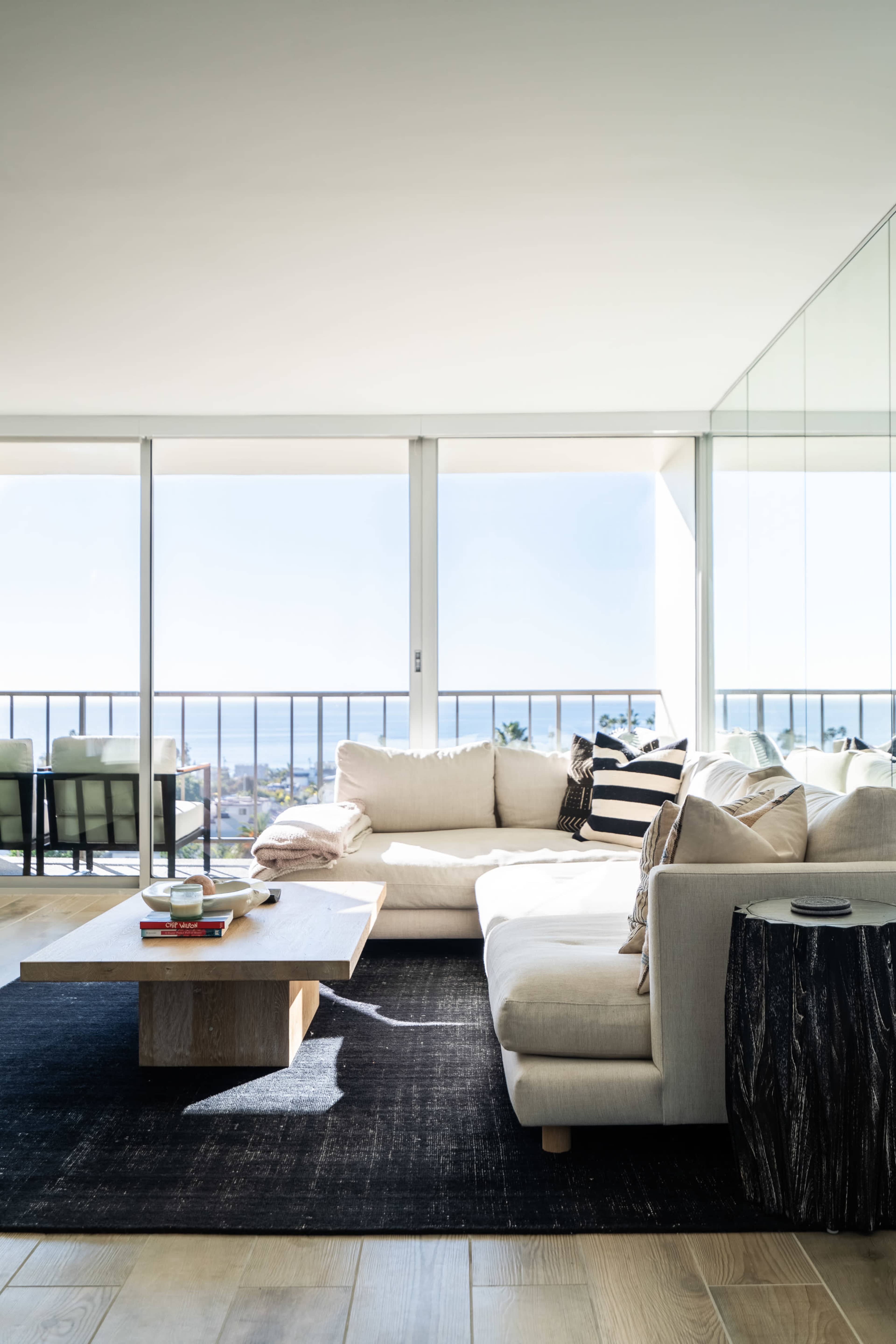 A modern living room with a large sectional sofa, a wooden coffee table, and a view of the ocean through large glass windows.