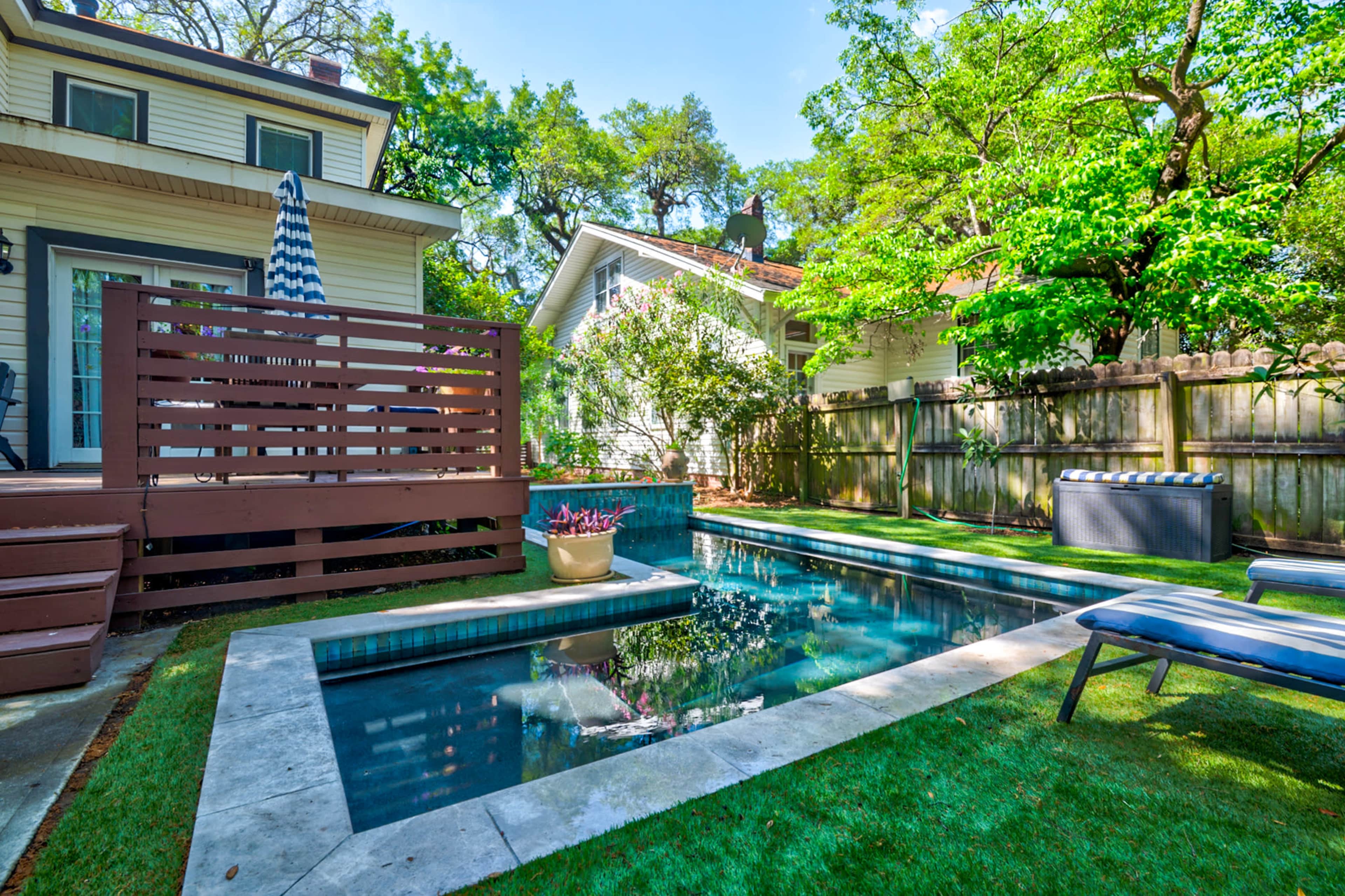 The image shows a backyard with a swimming pool, surrounded by greenery and a wooden deck.