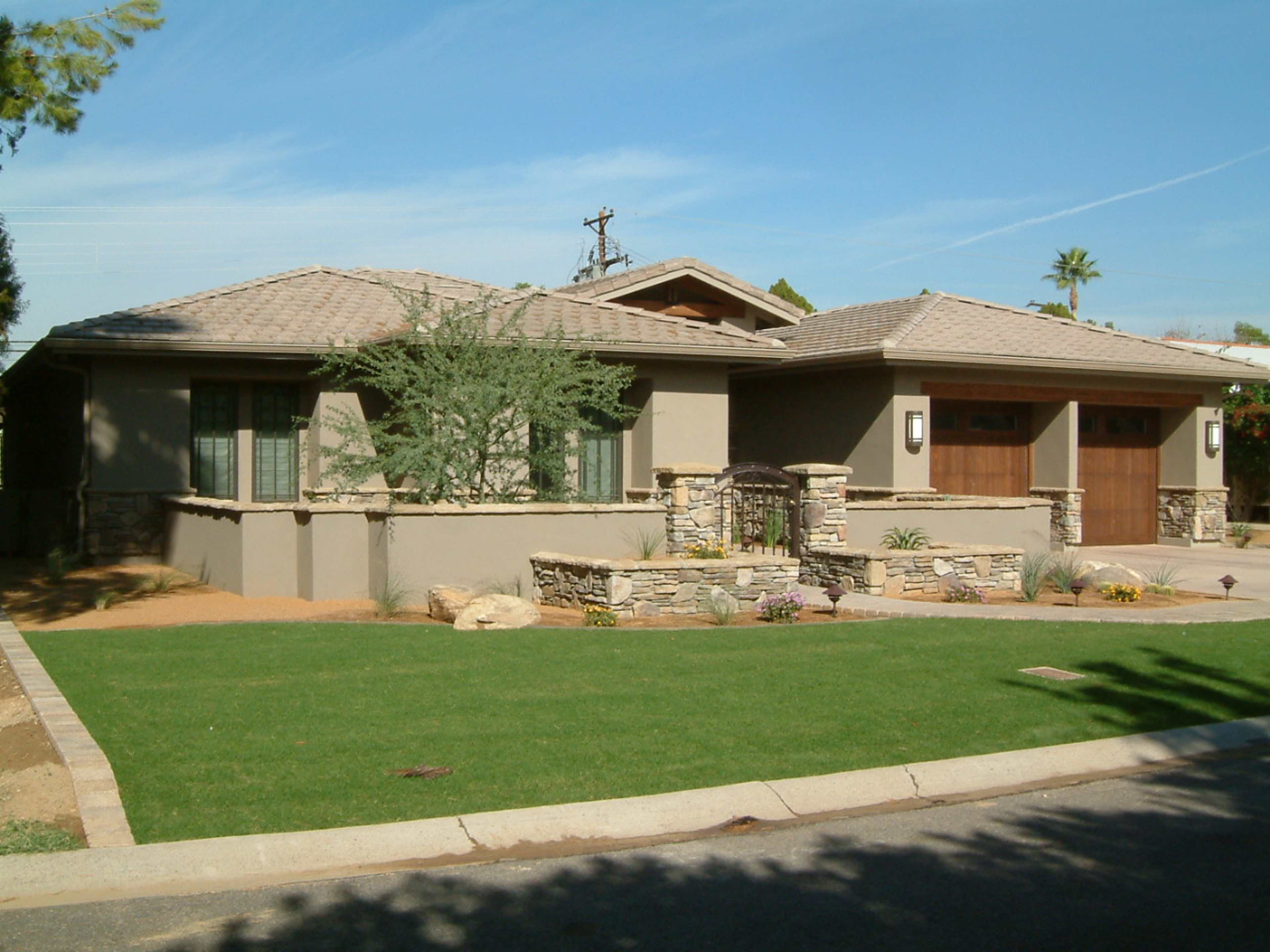 A modern single-story house with a stone facade, green lawn, and a two-car garage.