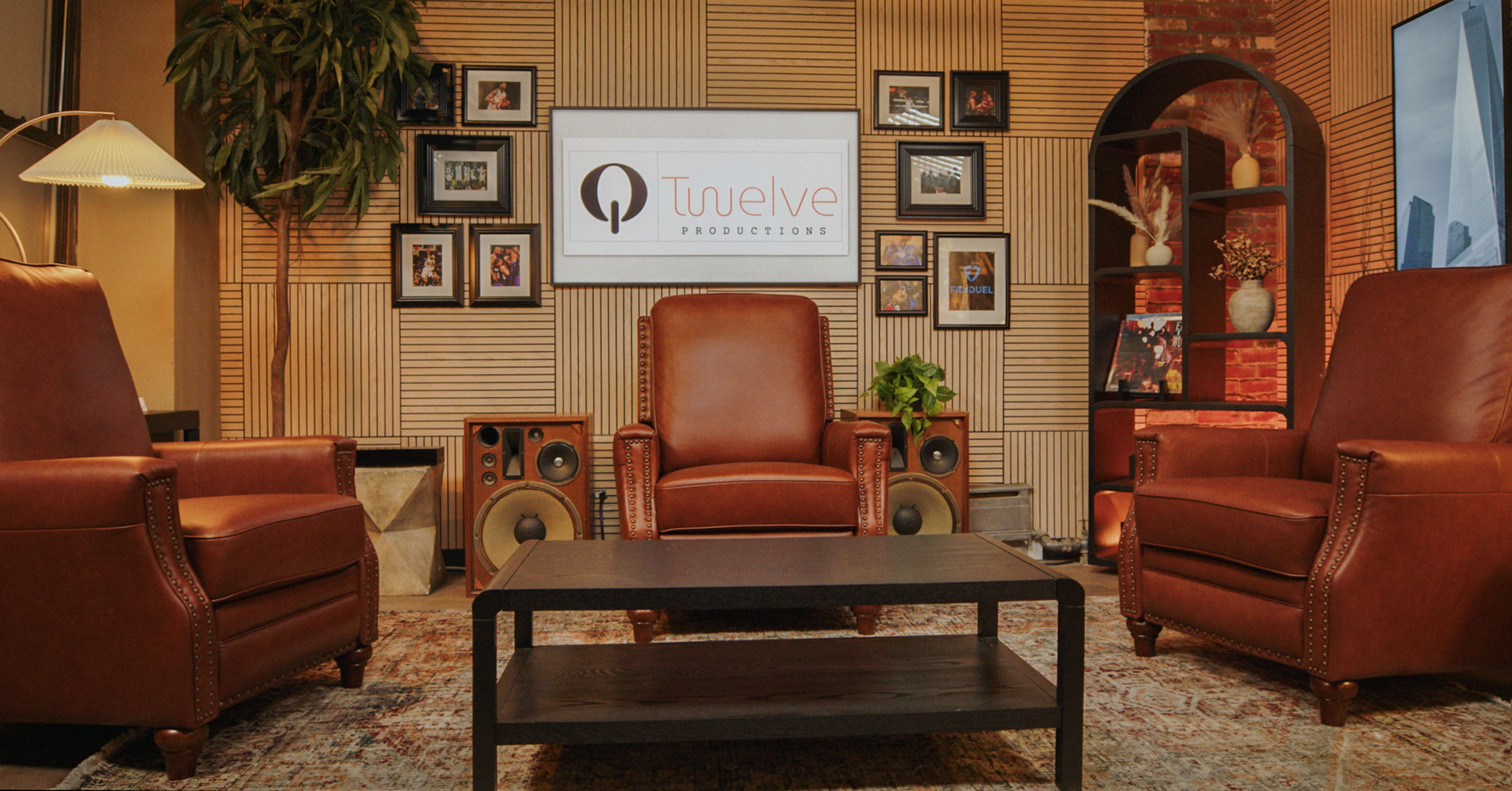 The image features a cozy studio setup with two brown leather armchairs facing a dark wooden coffee table, surrounded by decorative elements and a branded sign on the wall.