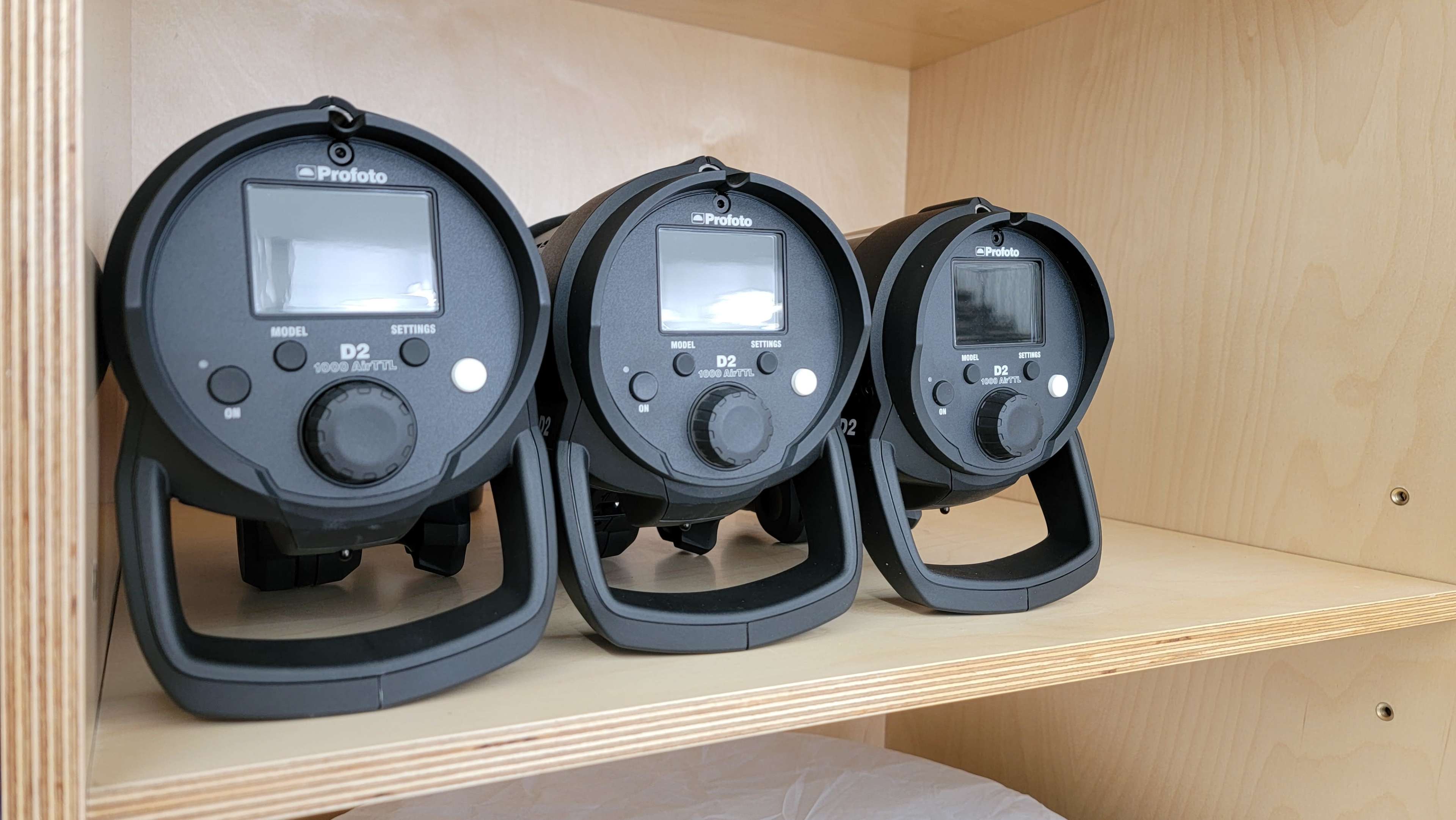 Three Profoto lighting units are arranged on a wooden shelf.