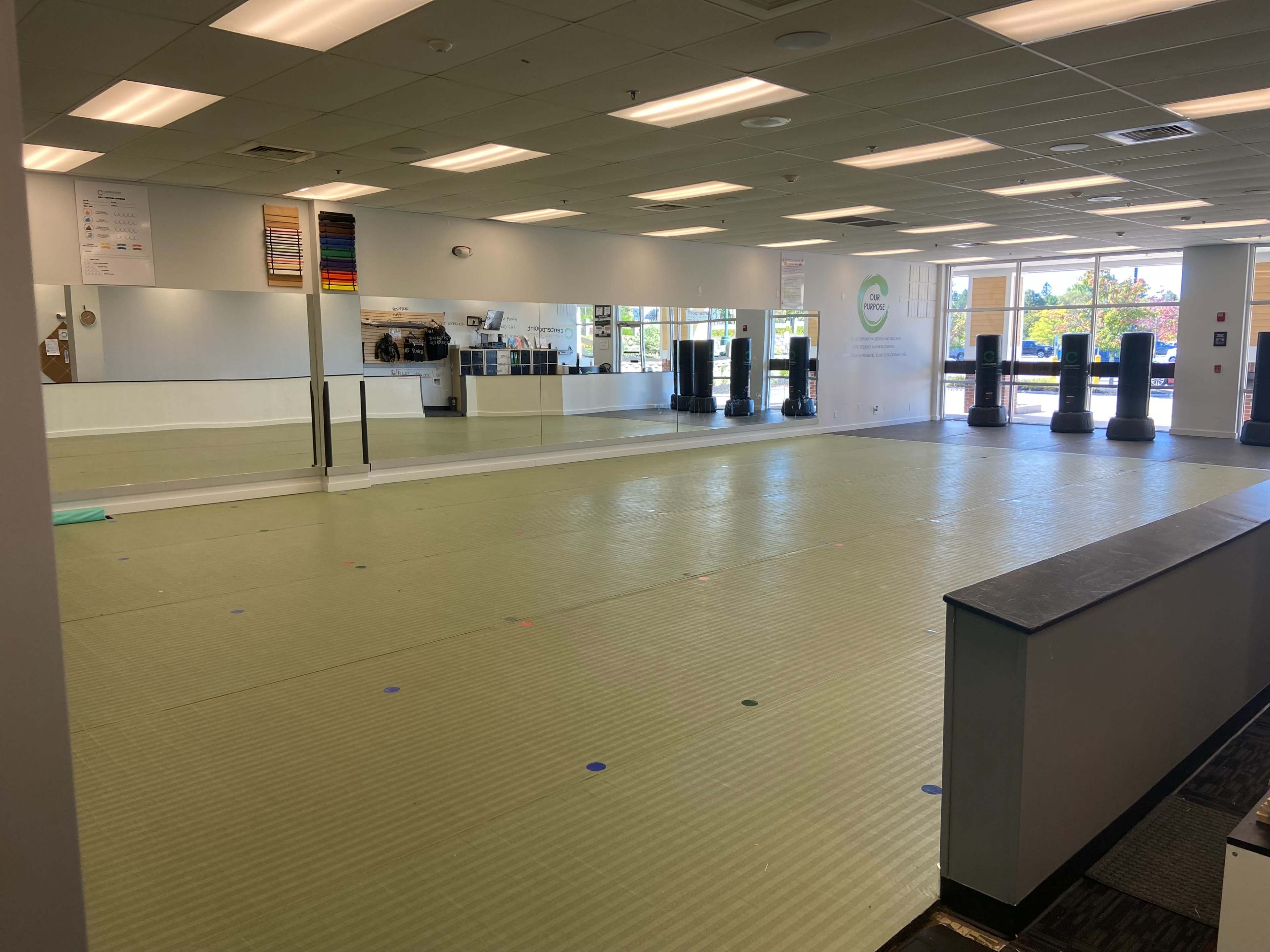 A spacious, empty fitness studio with mirrored walls and exercise mats, featuring various fitness equipment in the background.