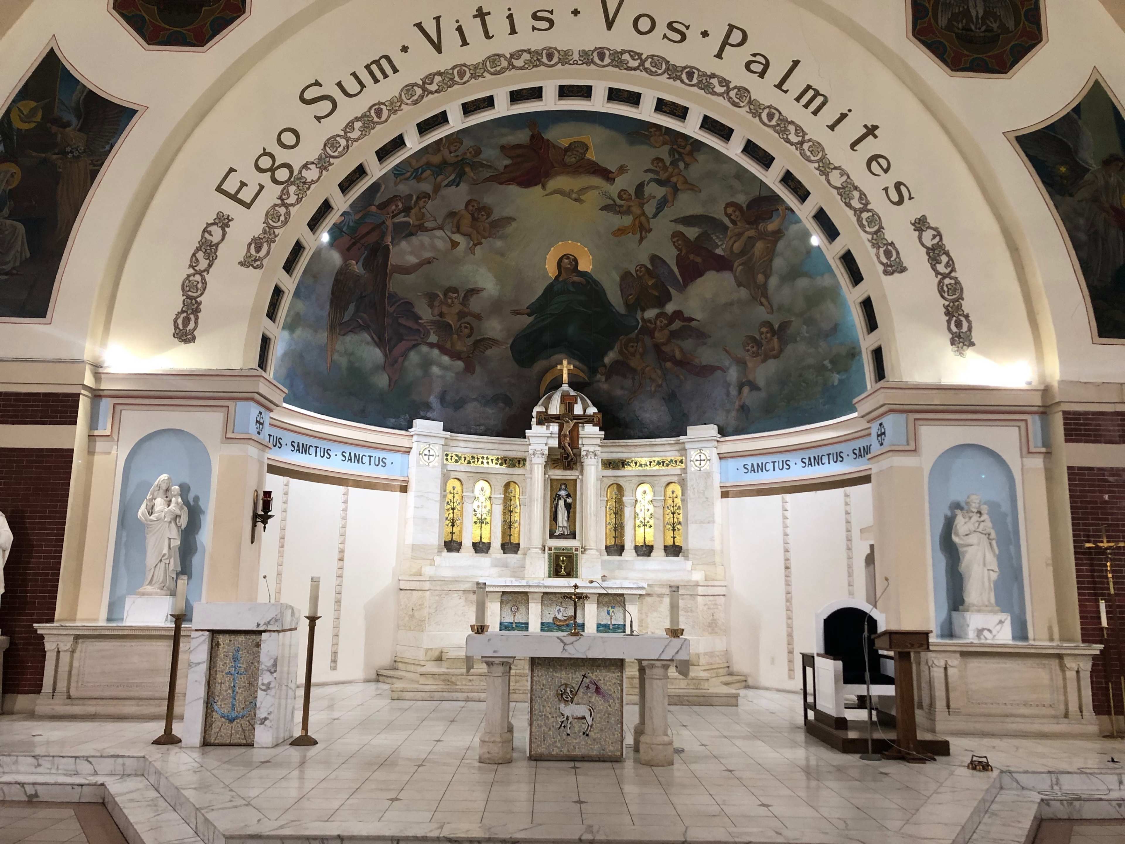 The interior of a church featuring an ornate altar with a large mural above it, surrounded by statues and decorative elements.