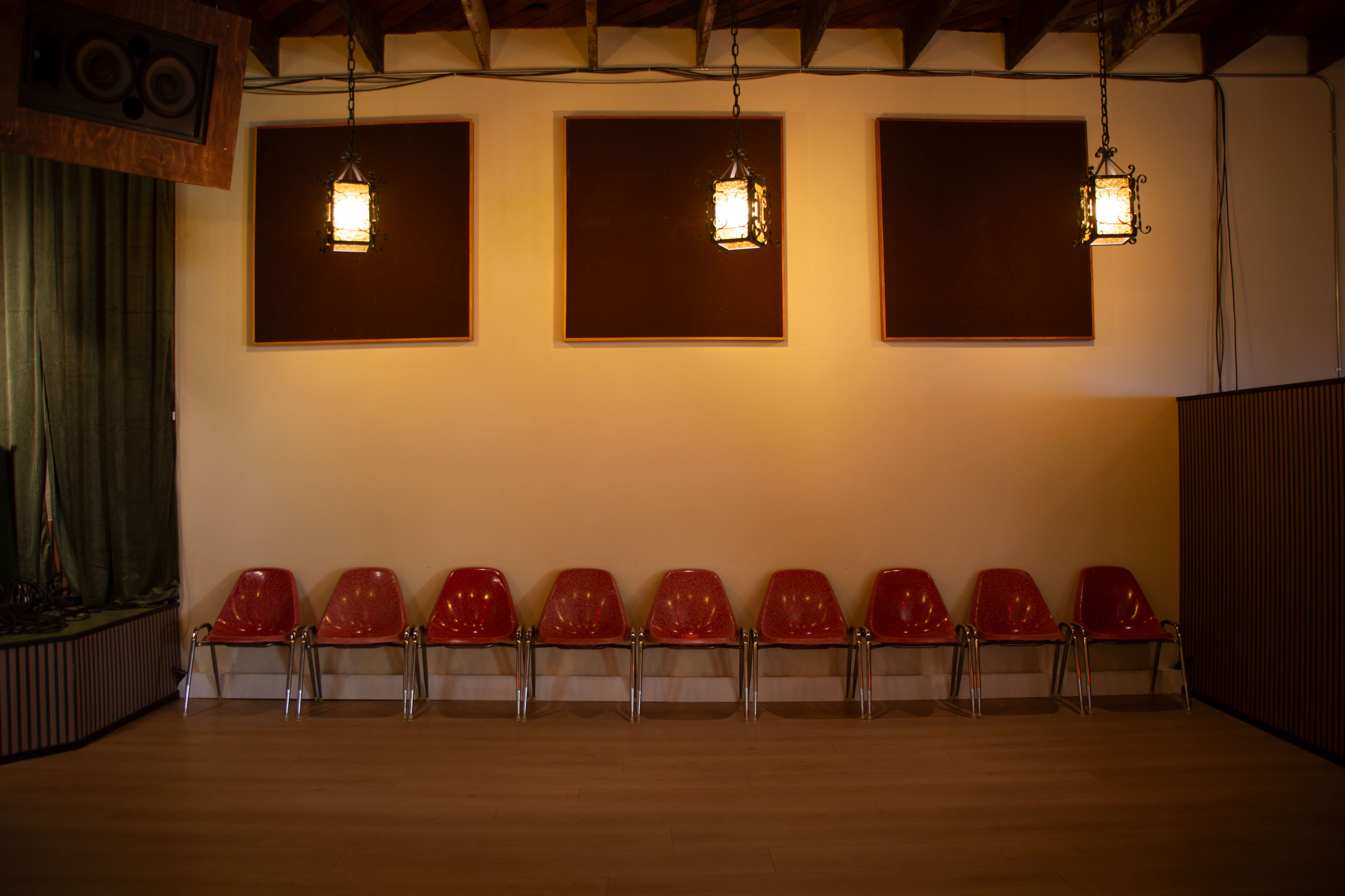 The image shows a row of red chairs arranged neatly against a plain wall, illuminated by warm light from two hanging lanterns above.