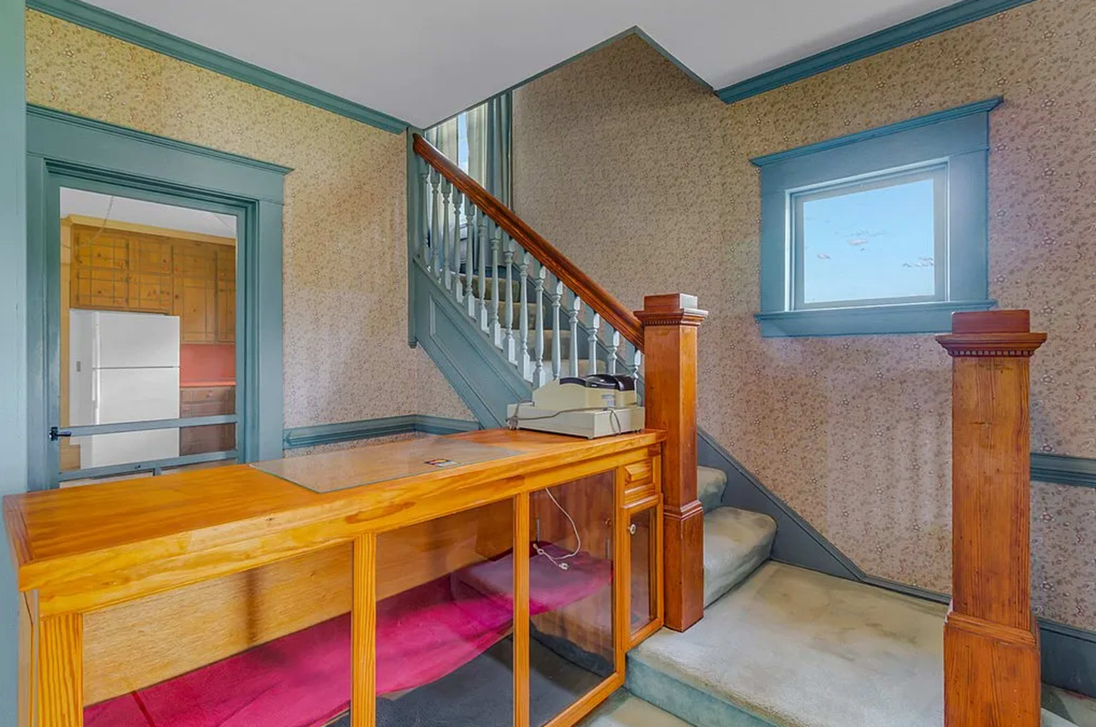 The image shows an entrance hallway featuring a wooden reception desk, a staircase leading to the upper floor, and a window allowing natural light.