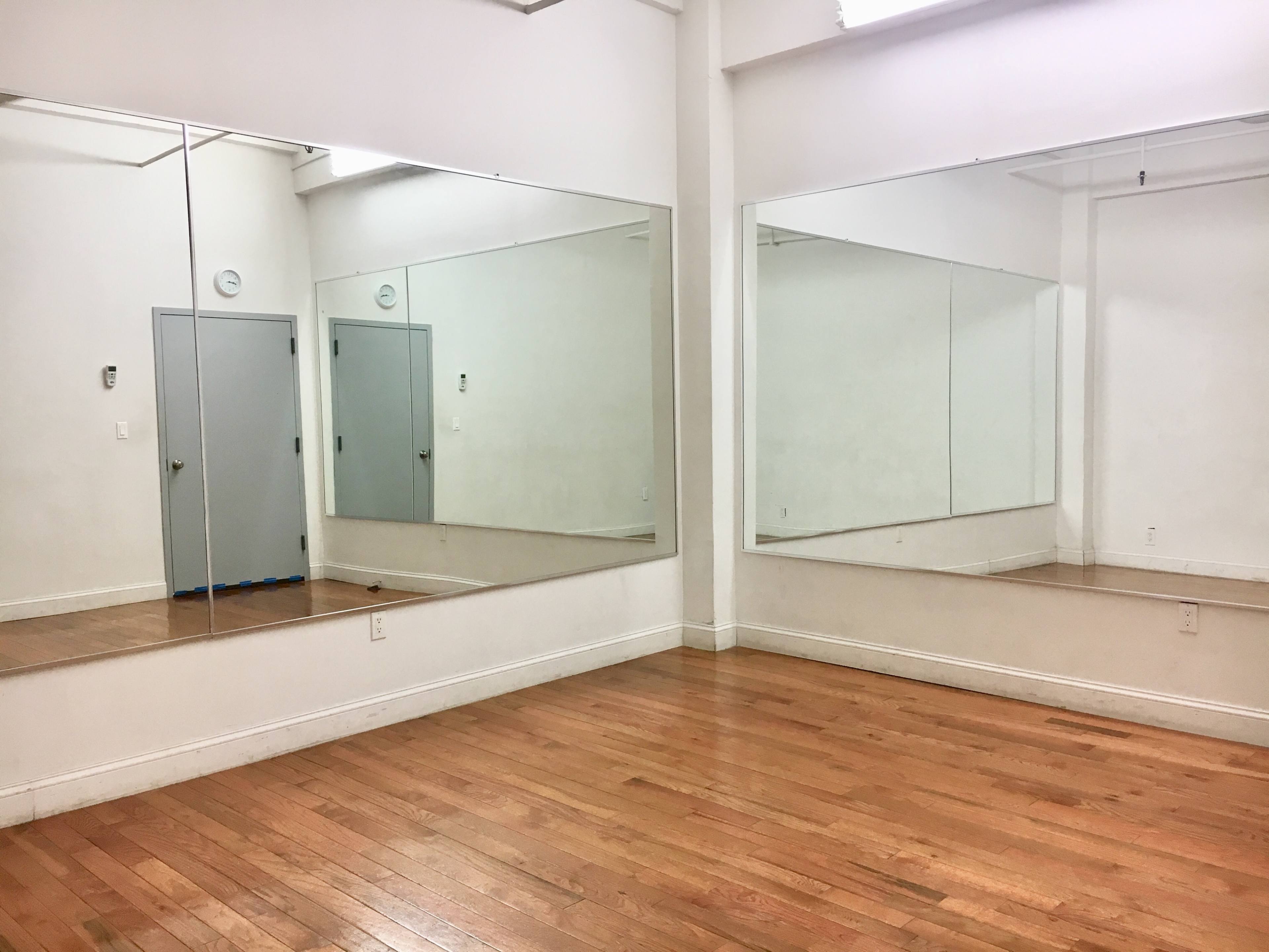 A bright, empty room with wooden floors and two large mirrors on opposing walls.