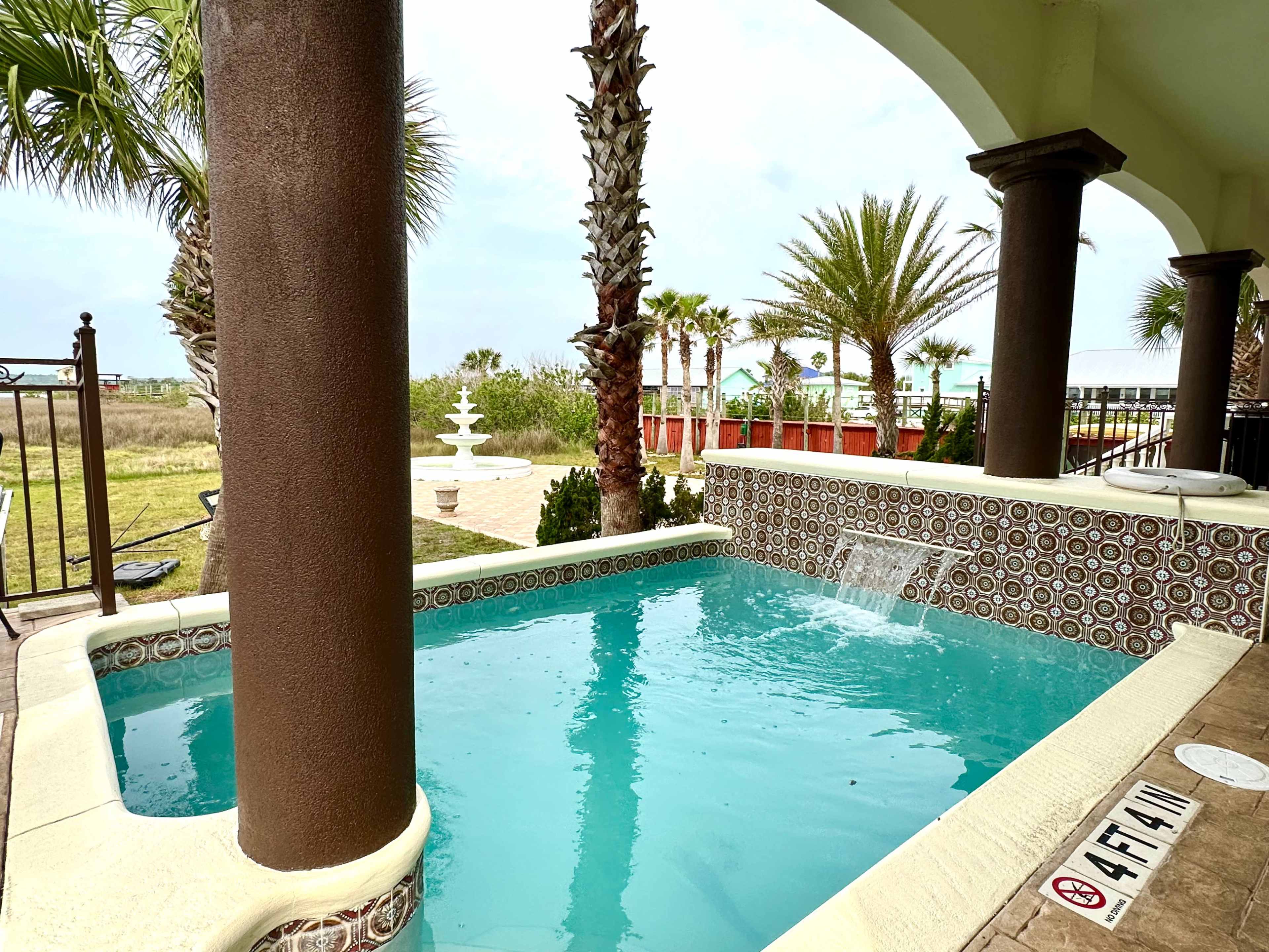 A small swimming pool surrounded by palm trees and a landscaped area.