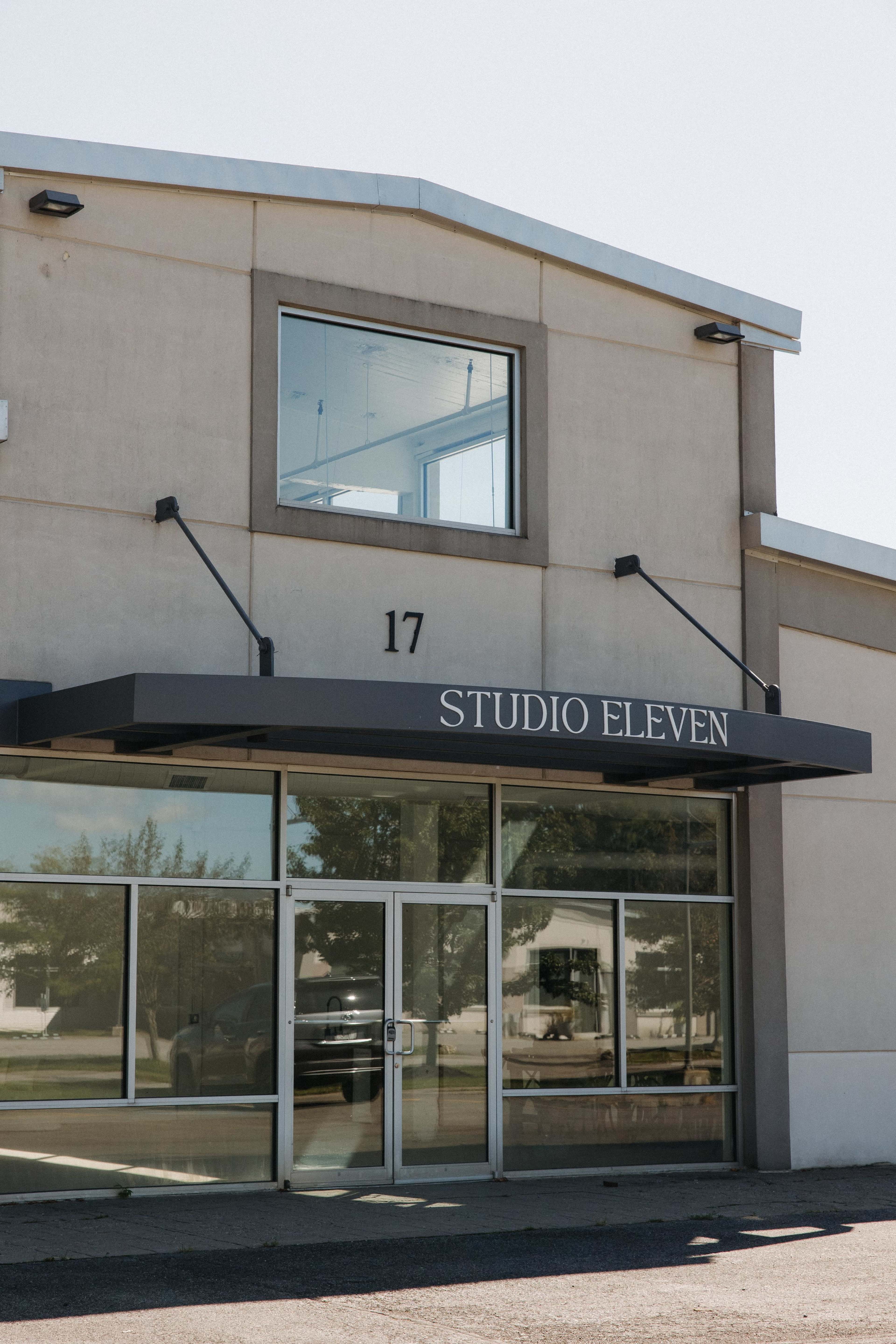 The image shows the exterior of a building labeled "STUDIO ELEVEN" with a large glass entrance and a number "17" above the doorway.