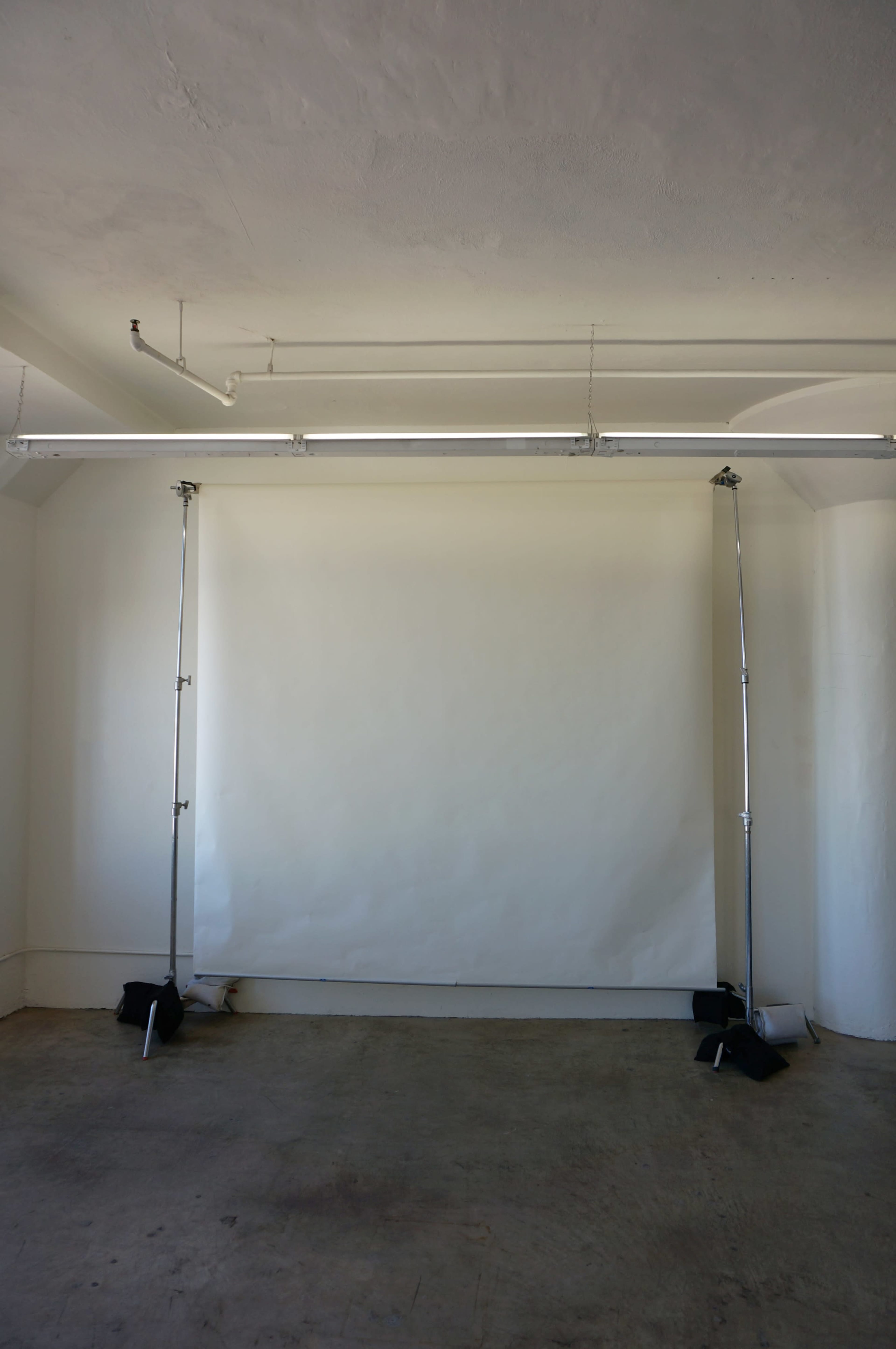 The image shows an empty room with two tall light stands supporting a white backdrop.