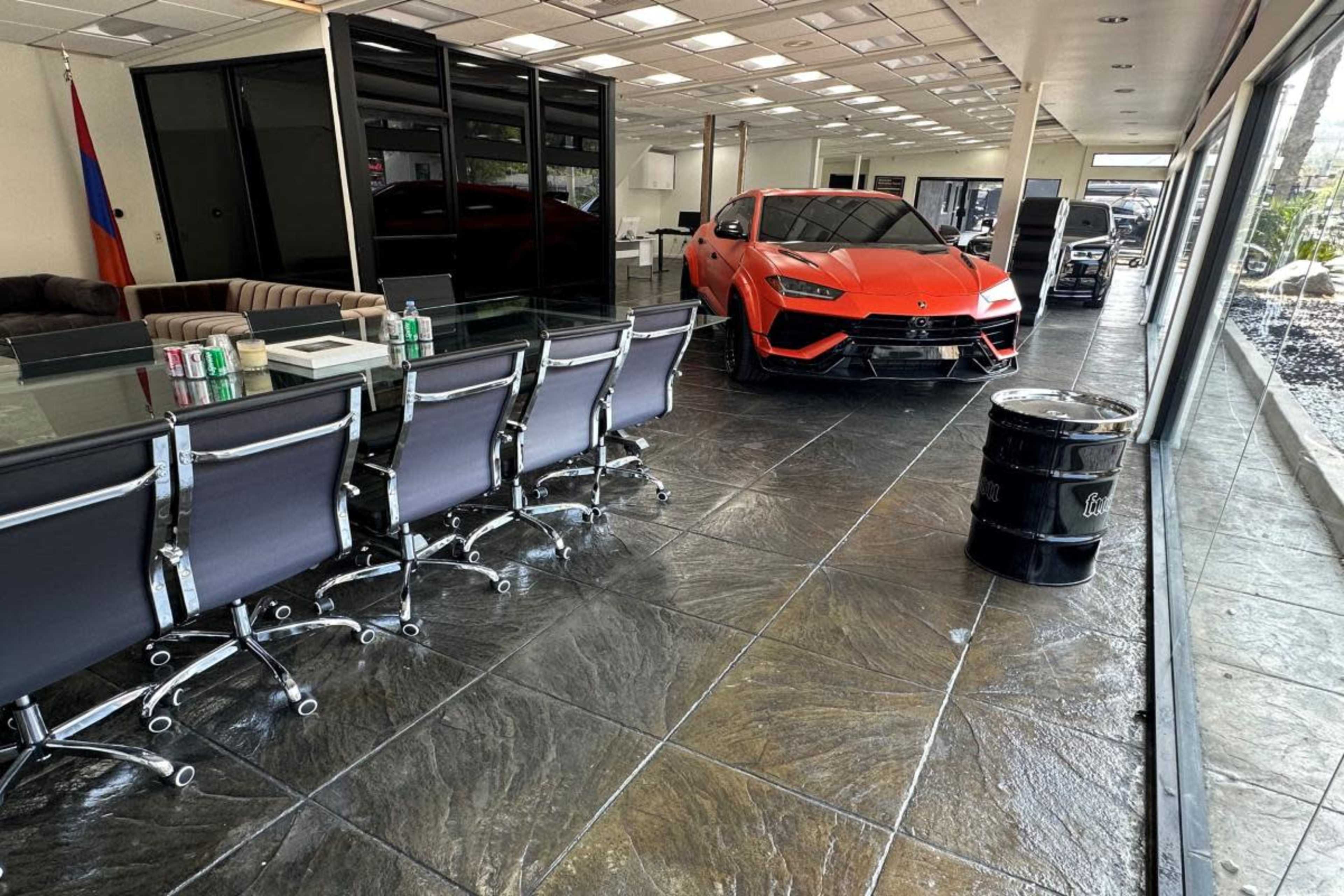 A sleek orange Lamborghini is prominently parked inside a modern office space with glass walls and a long conference table.