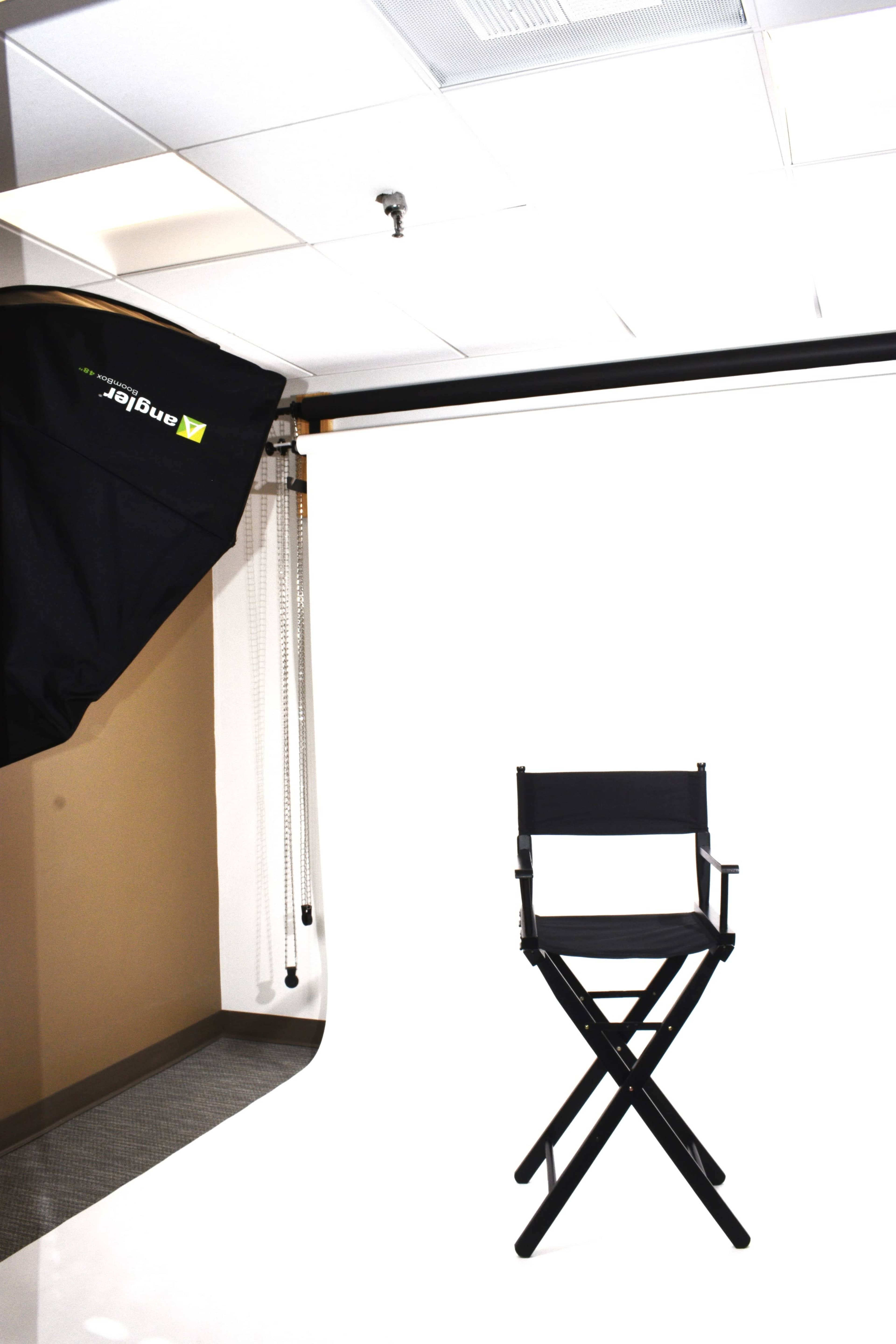 A photography studio setup with a black director's chair in front of a white backdrop and a softbox lighting equipment overhead.
