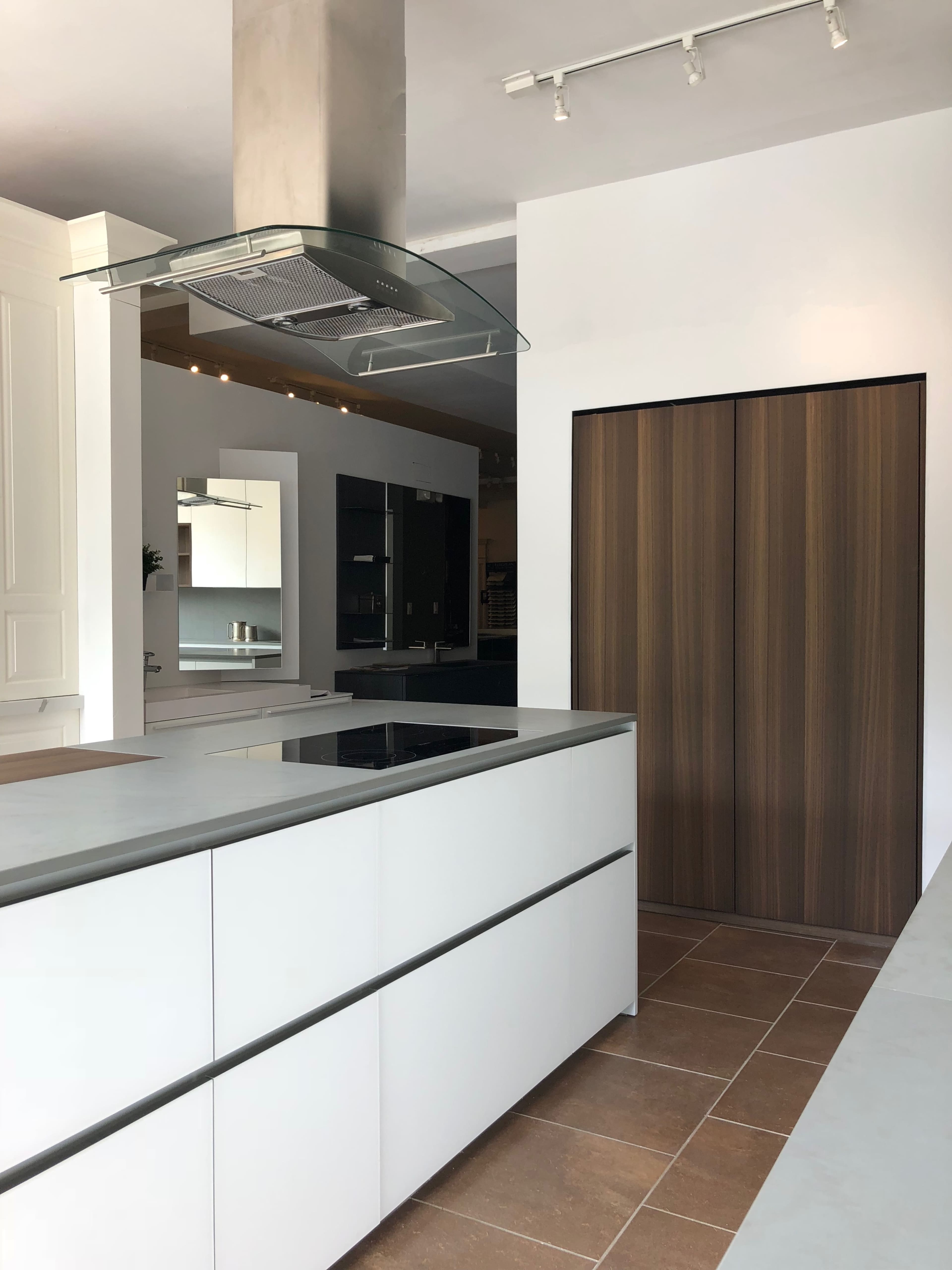 A modern kitchen features a large central island with a stovetop, sleek cabinetry, and a double-door wooden pantry.