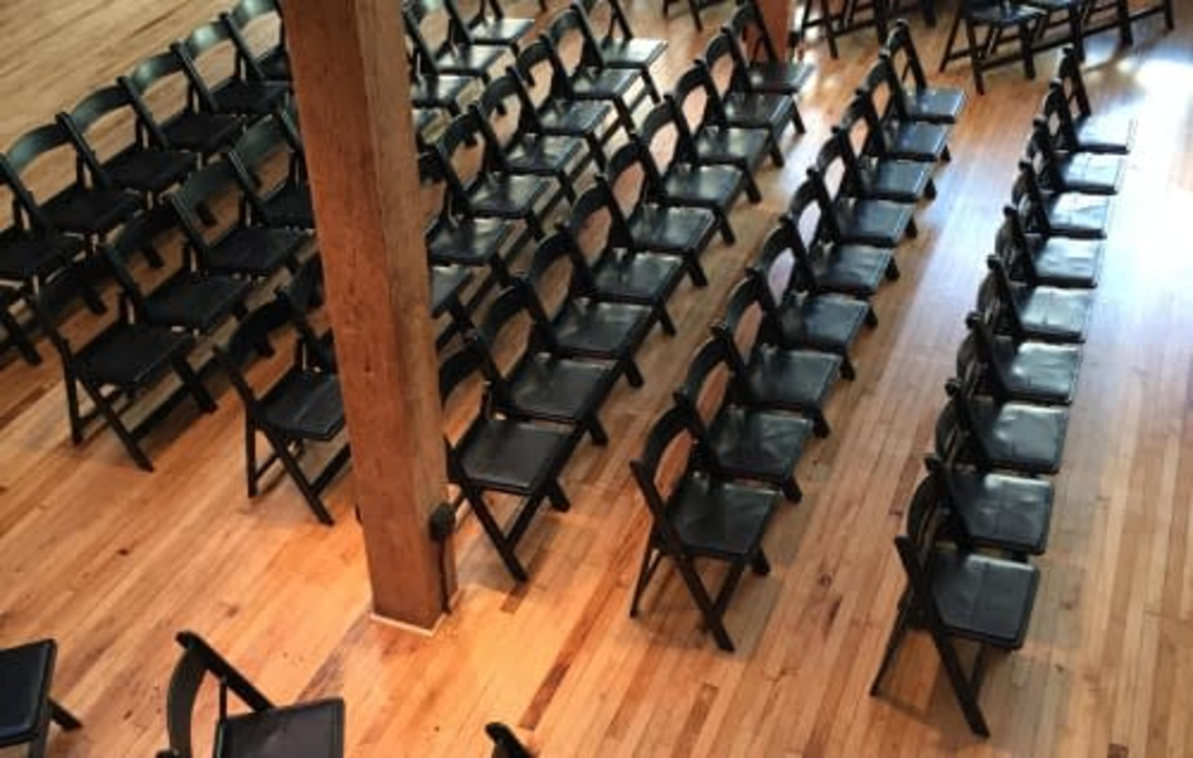 Neatly arranged black folding chairs set up on a wooden floor in a spacious venue.