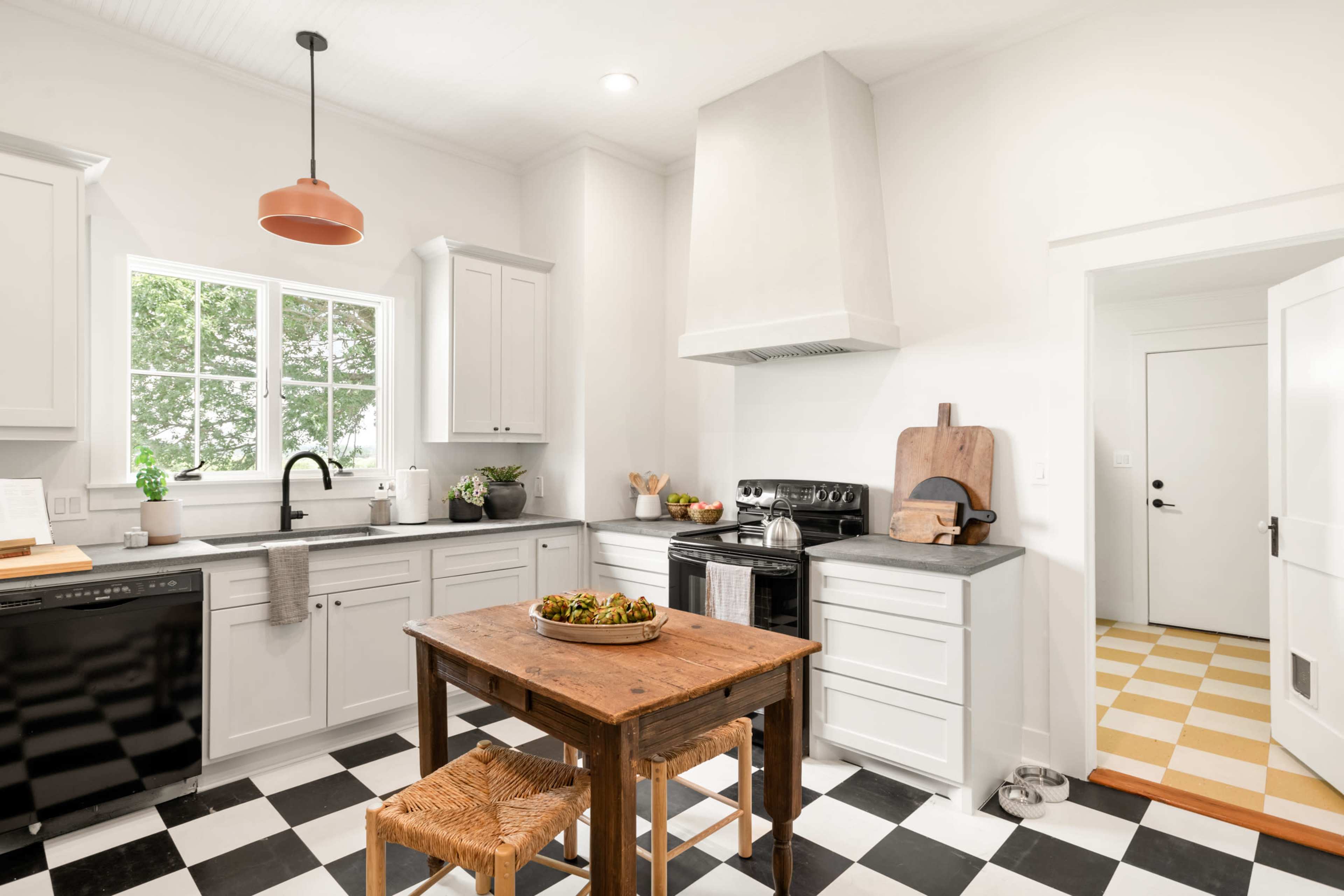 A modern kitchen with gray cabinetry, a black and white checkered floor, and a wooden table at the center.