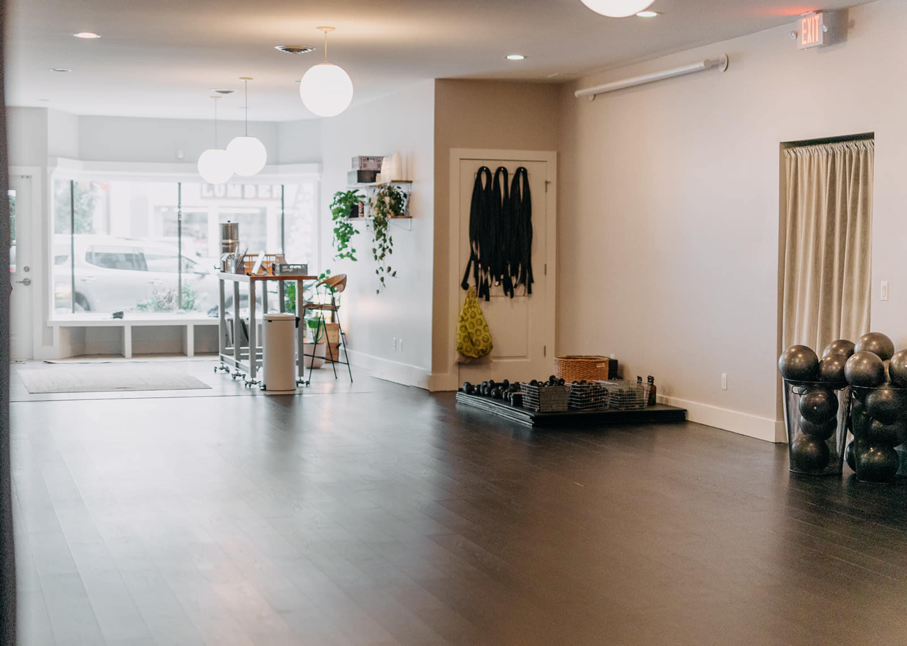 The image shows a spacious, well-lit fitness studio with exercise equipment, a reception area, and large windows.