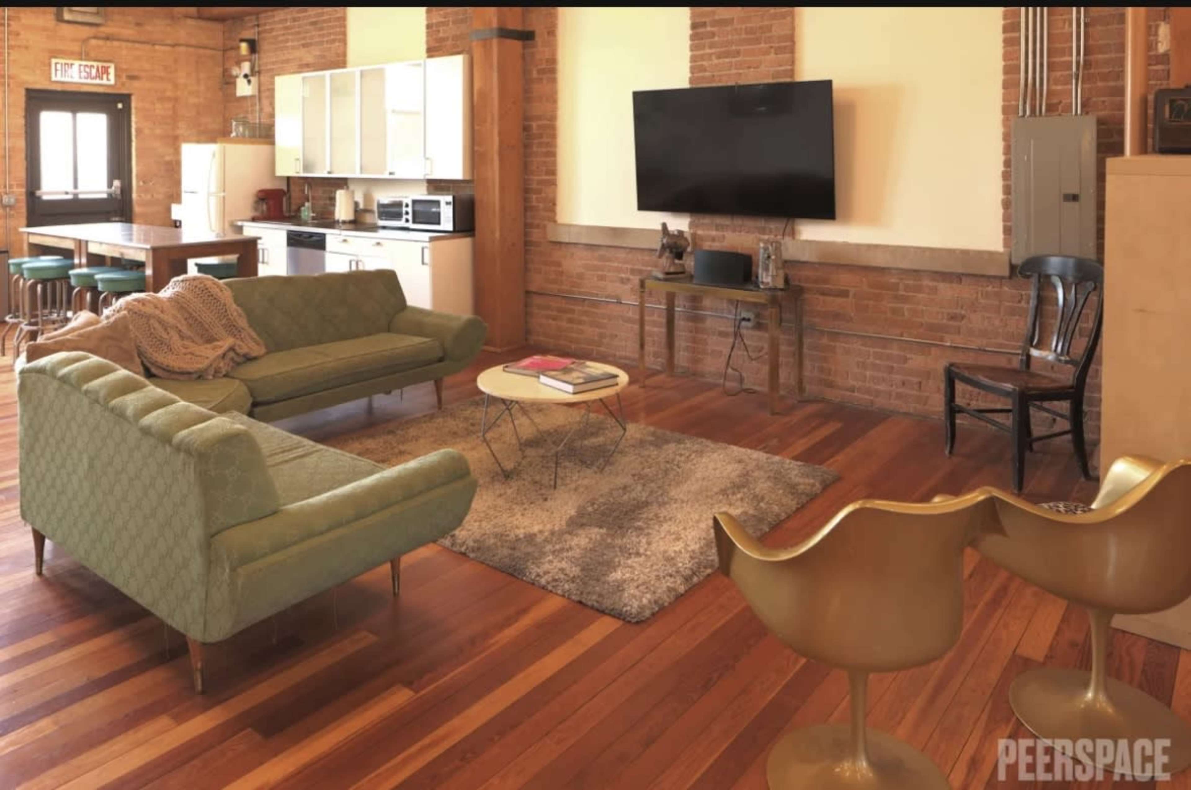 A spacious living area with a green couch, a round coffee table on a rug, a television mounted on the wall, and a kitchen area in the background.