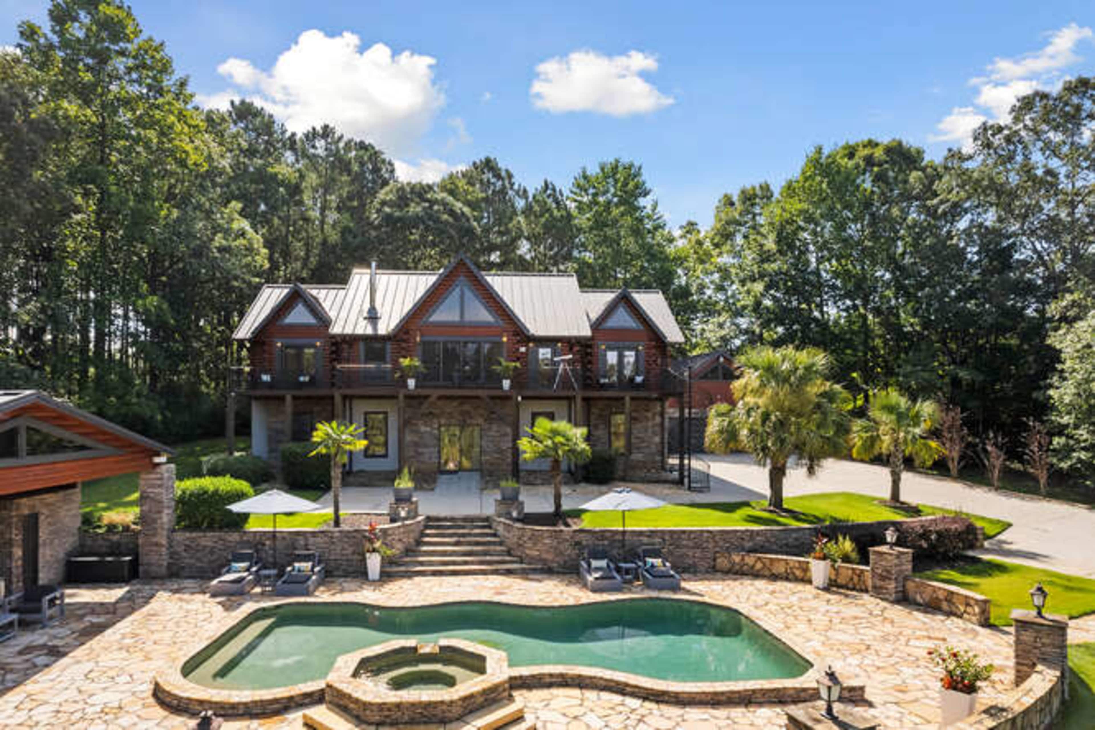 A large, modern house with a stone terrace and a swimming pool surrounded by landscaped greenery.