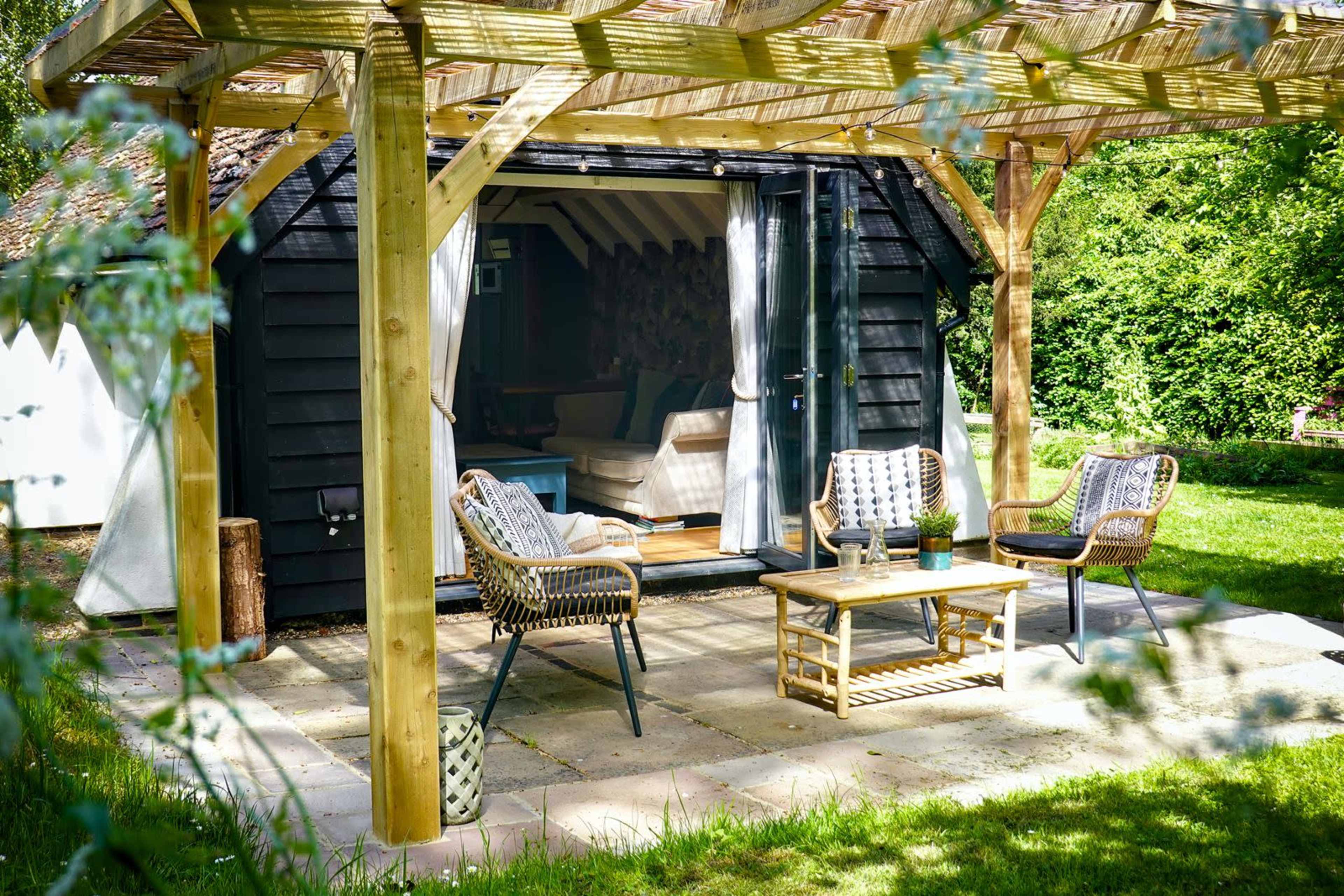 A cozy wooden patio features a table and chairs under a pergola, leading to an inviting indoor space with an open doorway.