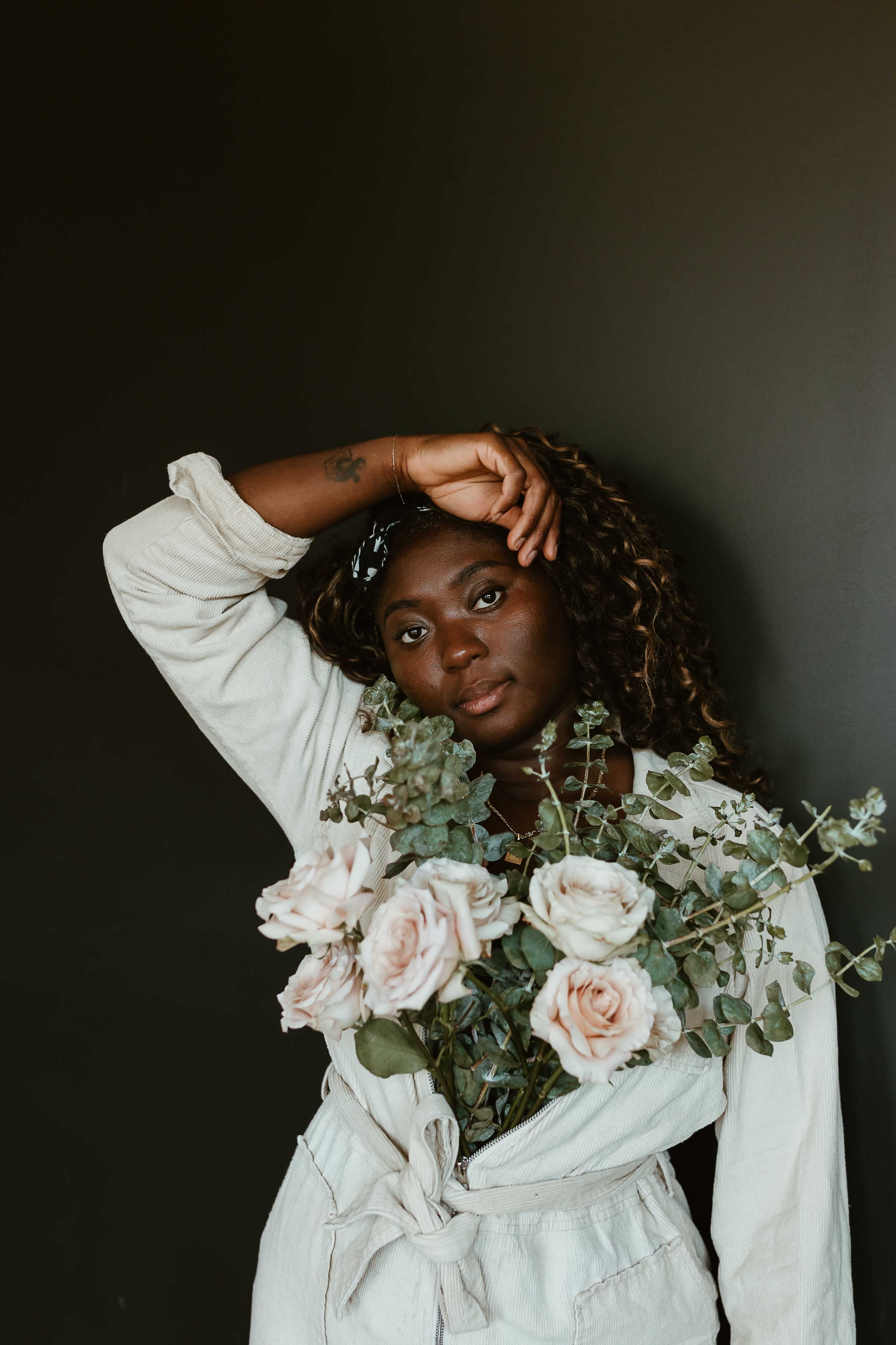 A person holds a bouquet of roses and greenery while posing against a dark background.