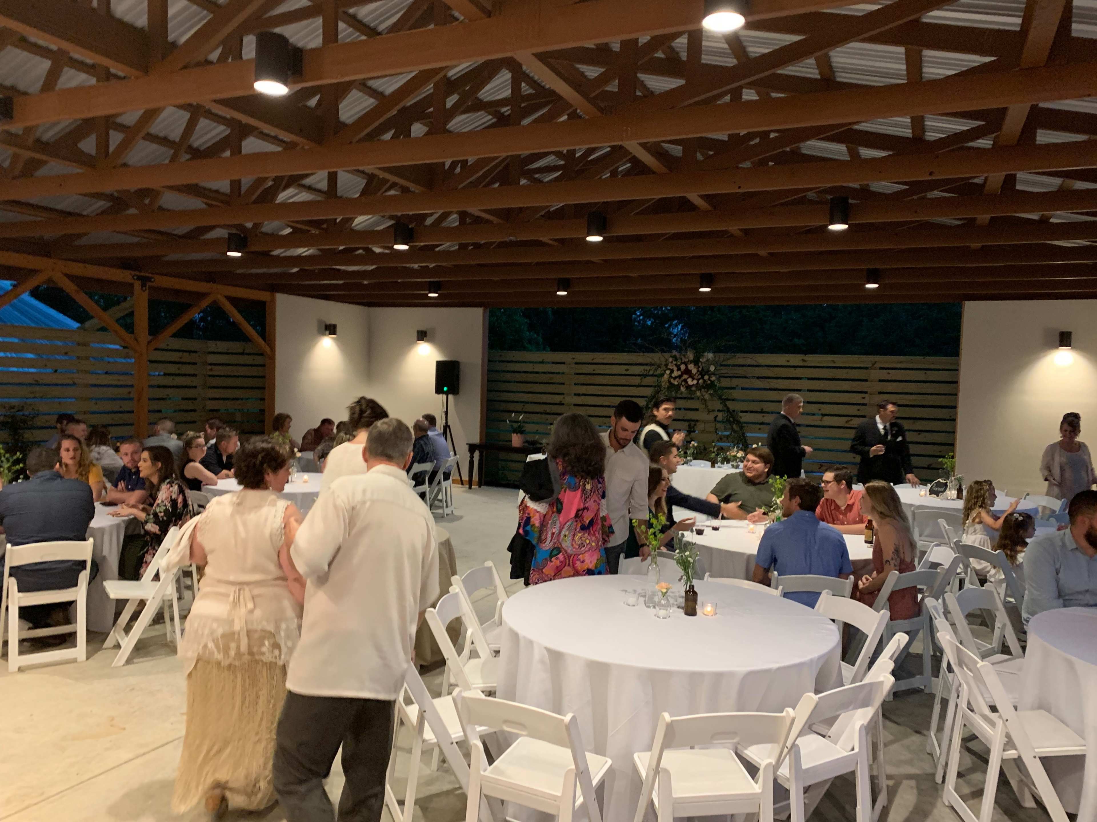 A spacious event space with round tables set for dining, where people are mingling and enjoying the evening.