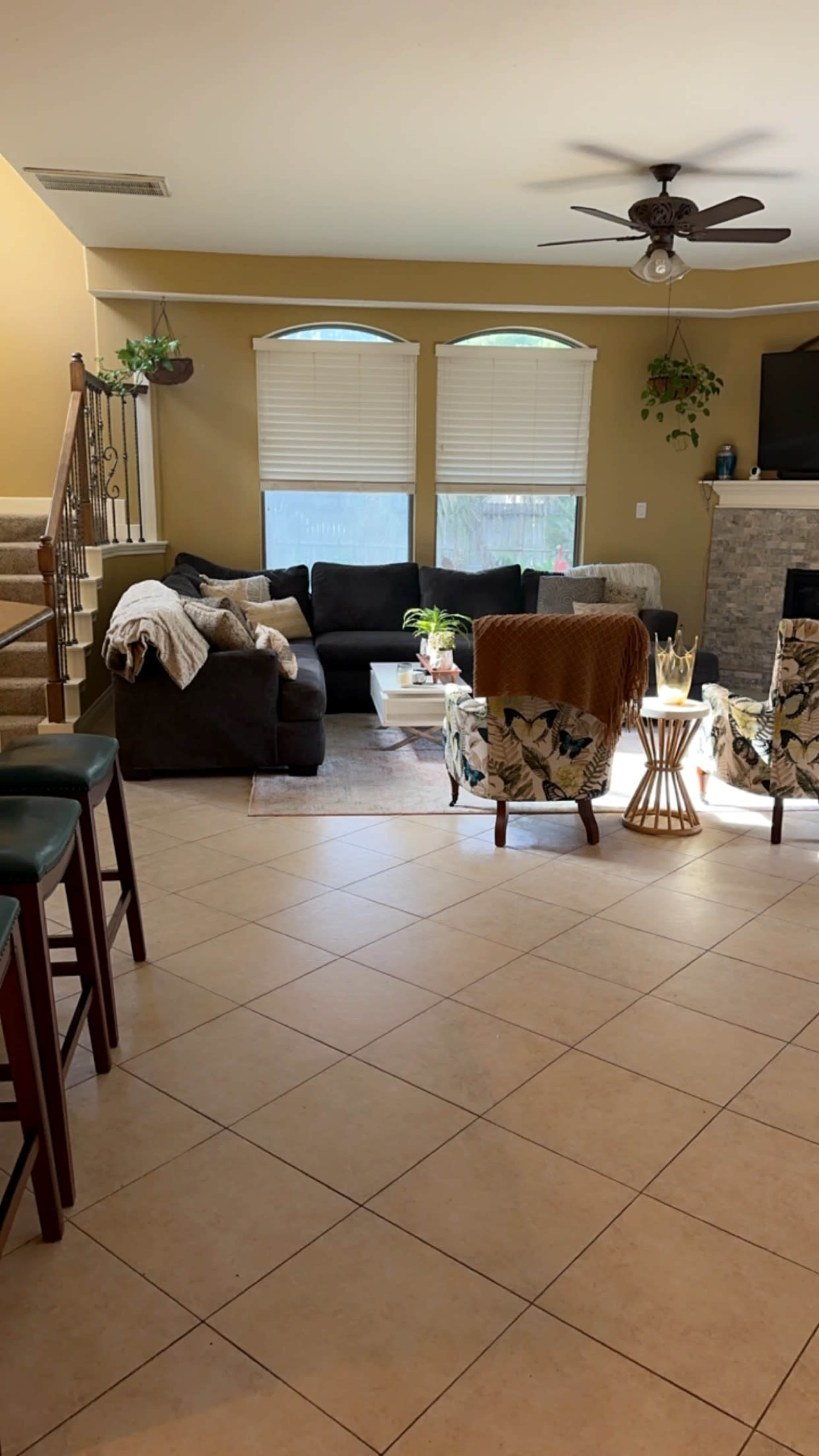 A living room area with a black sofa, two patterned chairs, a coffee table, and a staircase leading to an upper level.