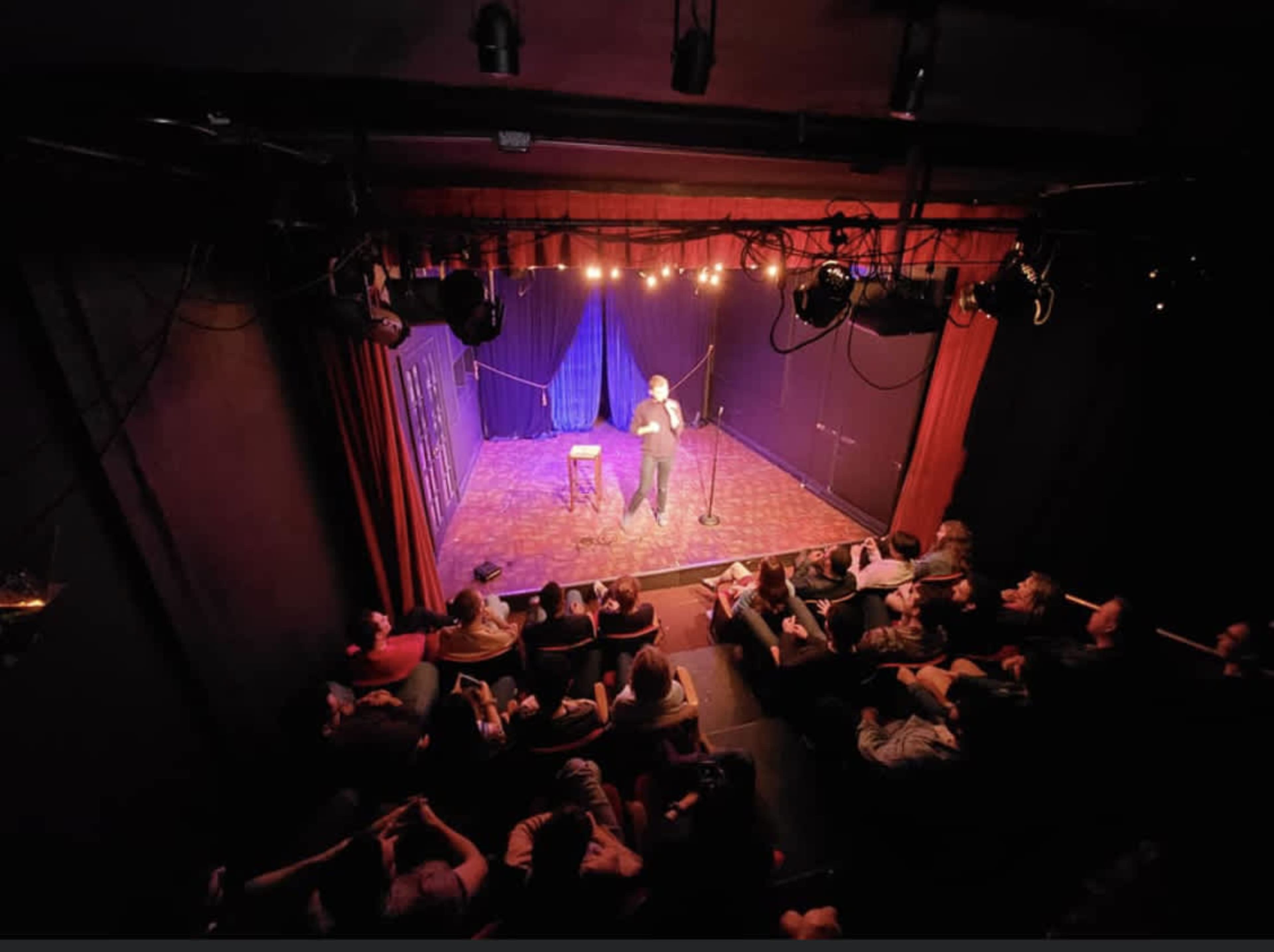 A comedian performs on stage in a small theater while an audience watches from their seats.