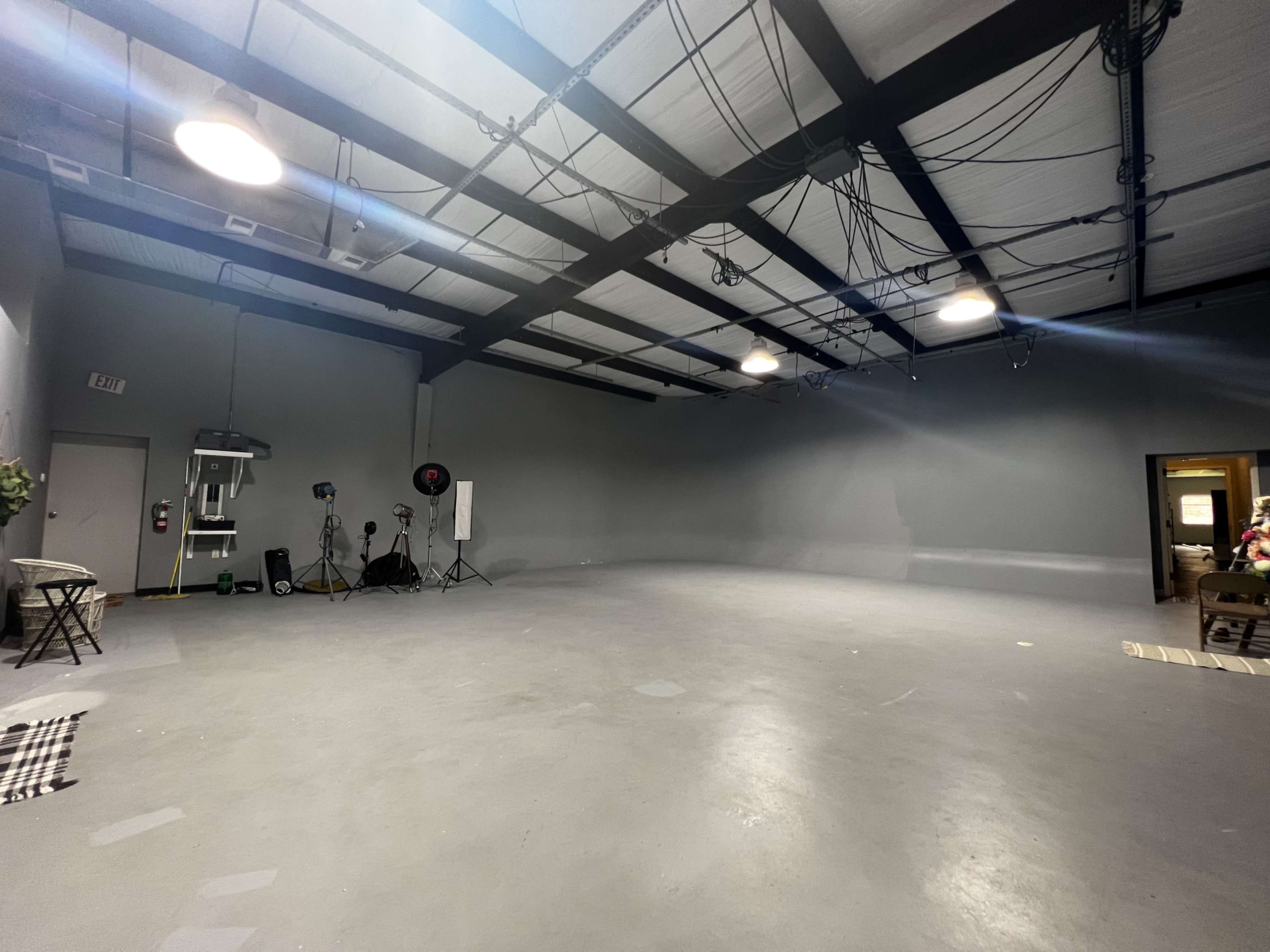 A spacious, empty interior room with gray walls, overhead lighting, and scattered photo equipment.