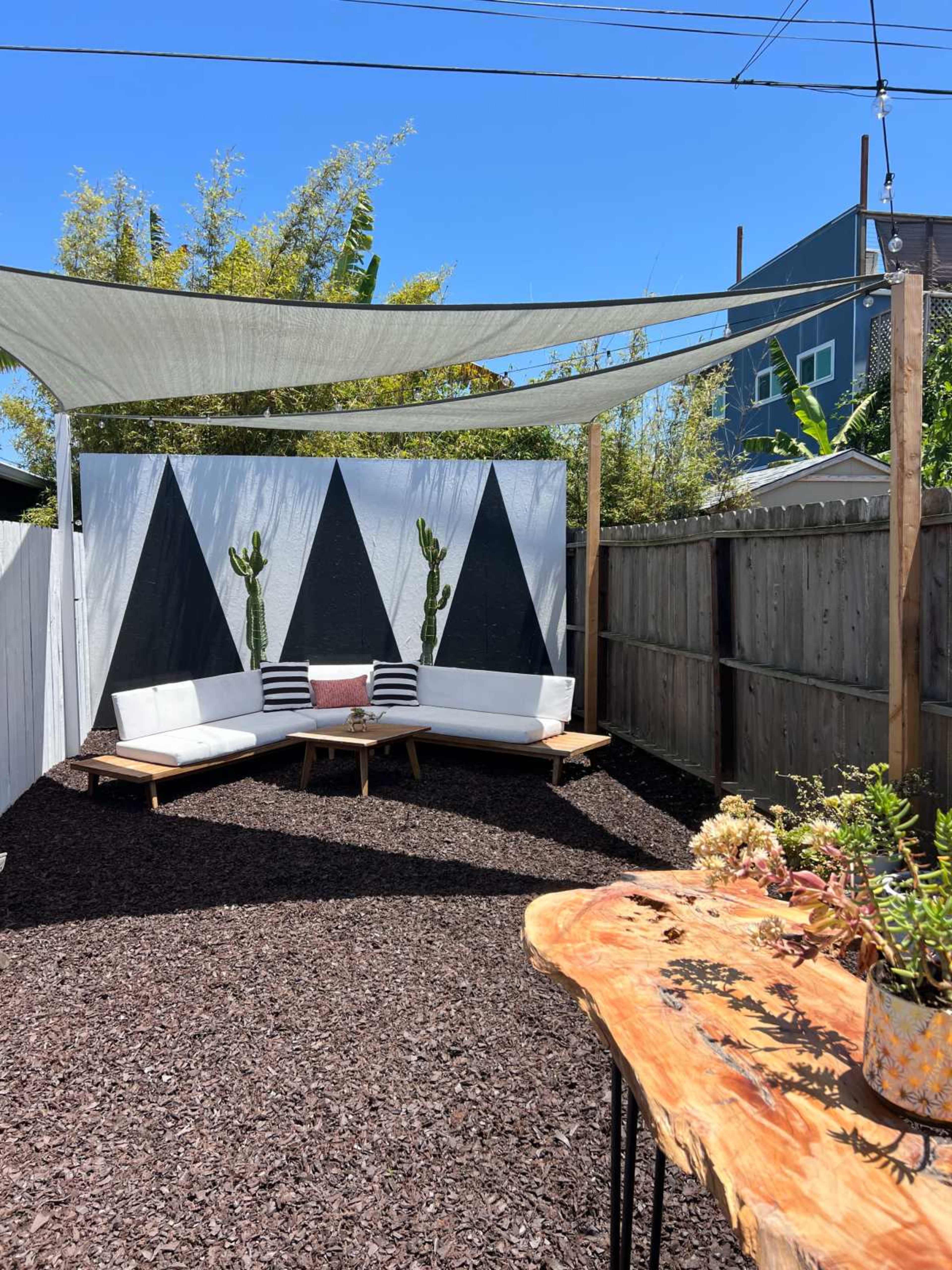 A shaded outdoor seating area with a wooden table and a wall featuring a black and white geometric design.