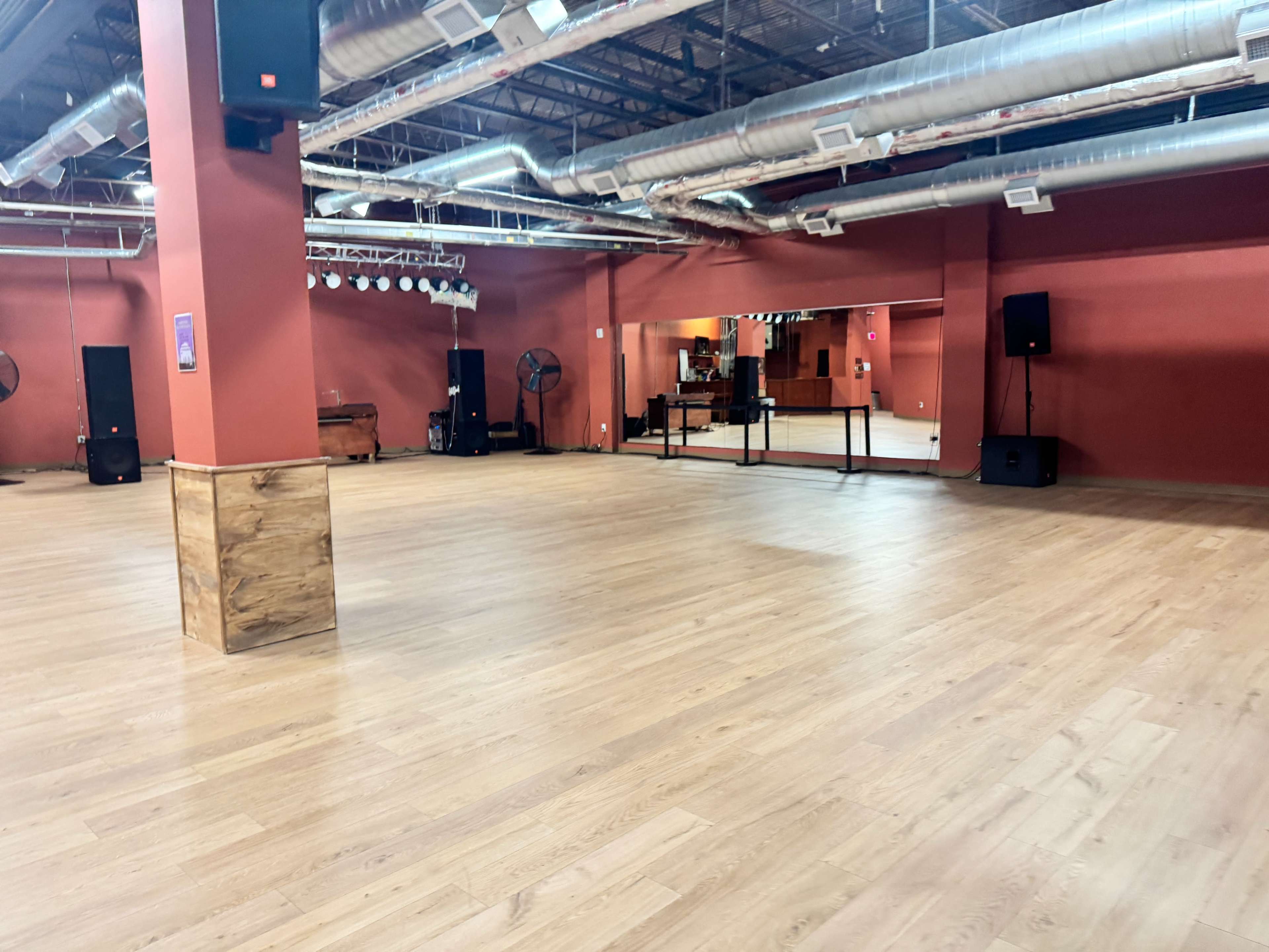 The image shows a spacious dance studio with wooden flooring, red walls, and sound equipment positioned around the room.
