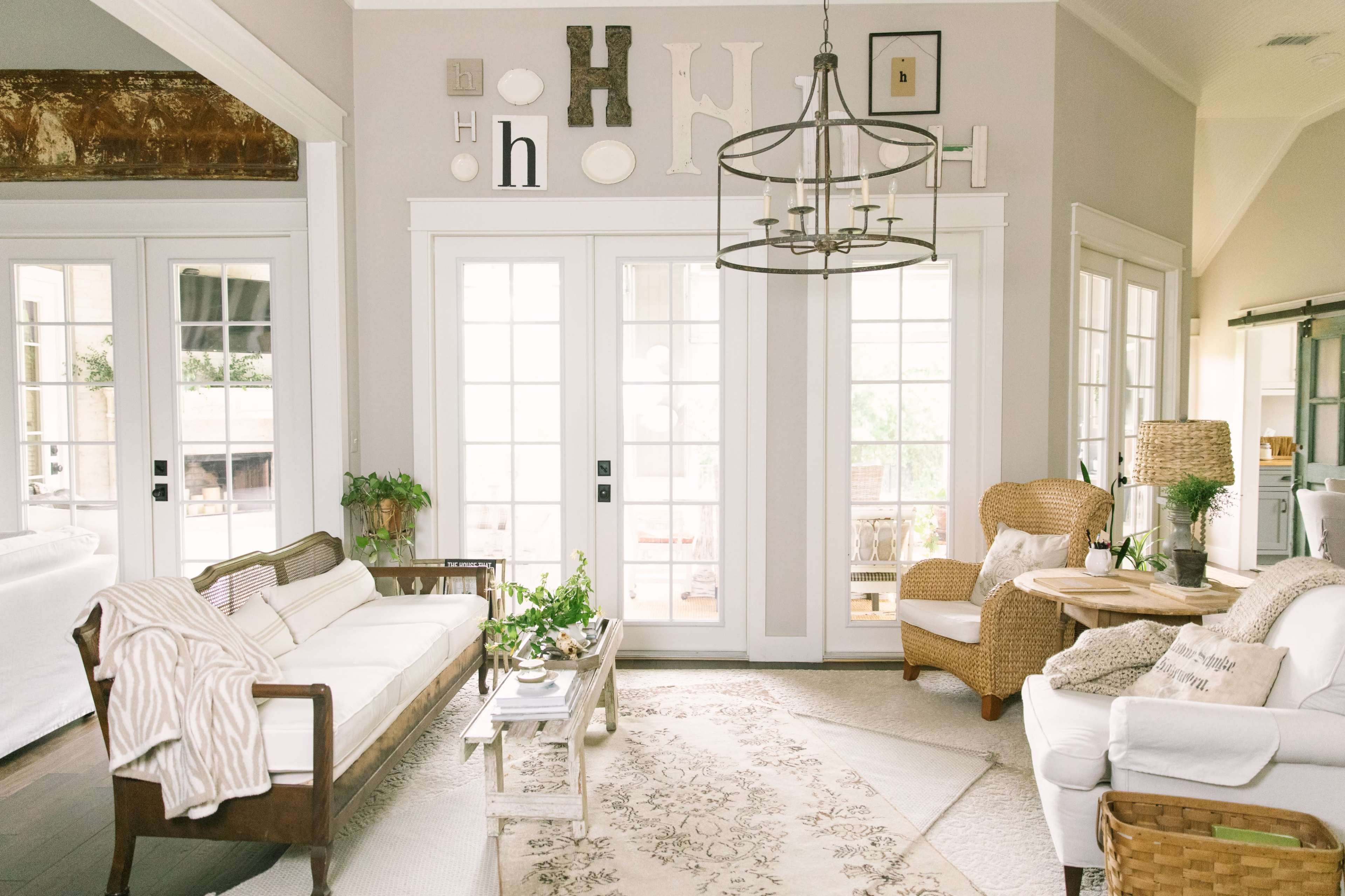 A bright living room features a mix of seating, decorative letters on the walls, and a large set of glass doors opening to an outdoor area.