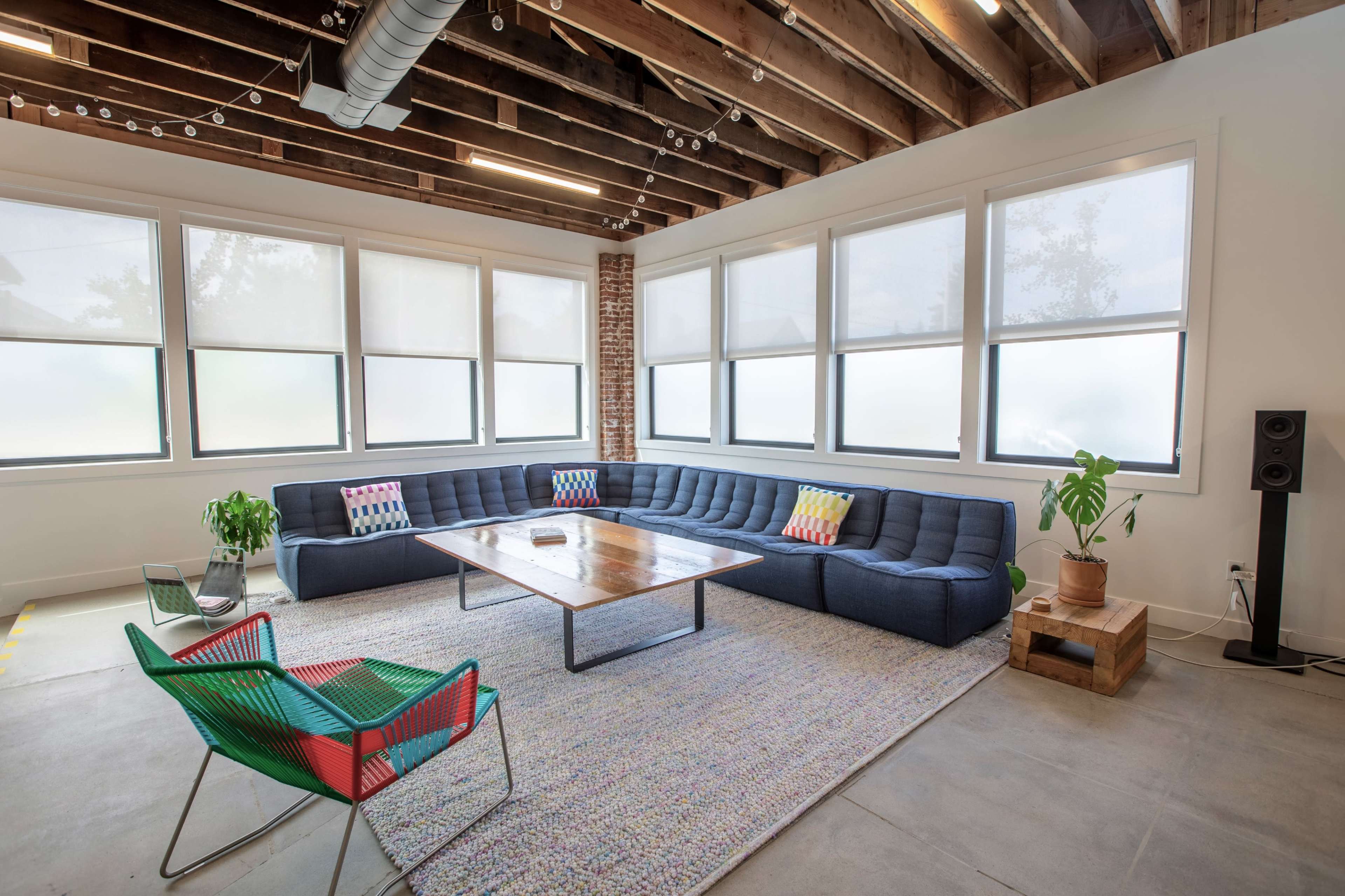 A modern, spacious living room with a large sectional sofa, a wooden coffee table, and several windows allowing natural light to enter.