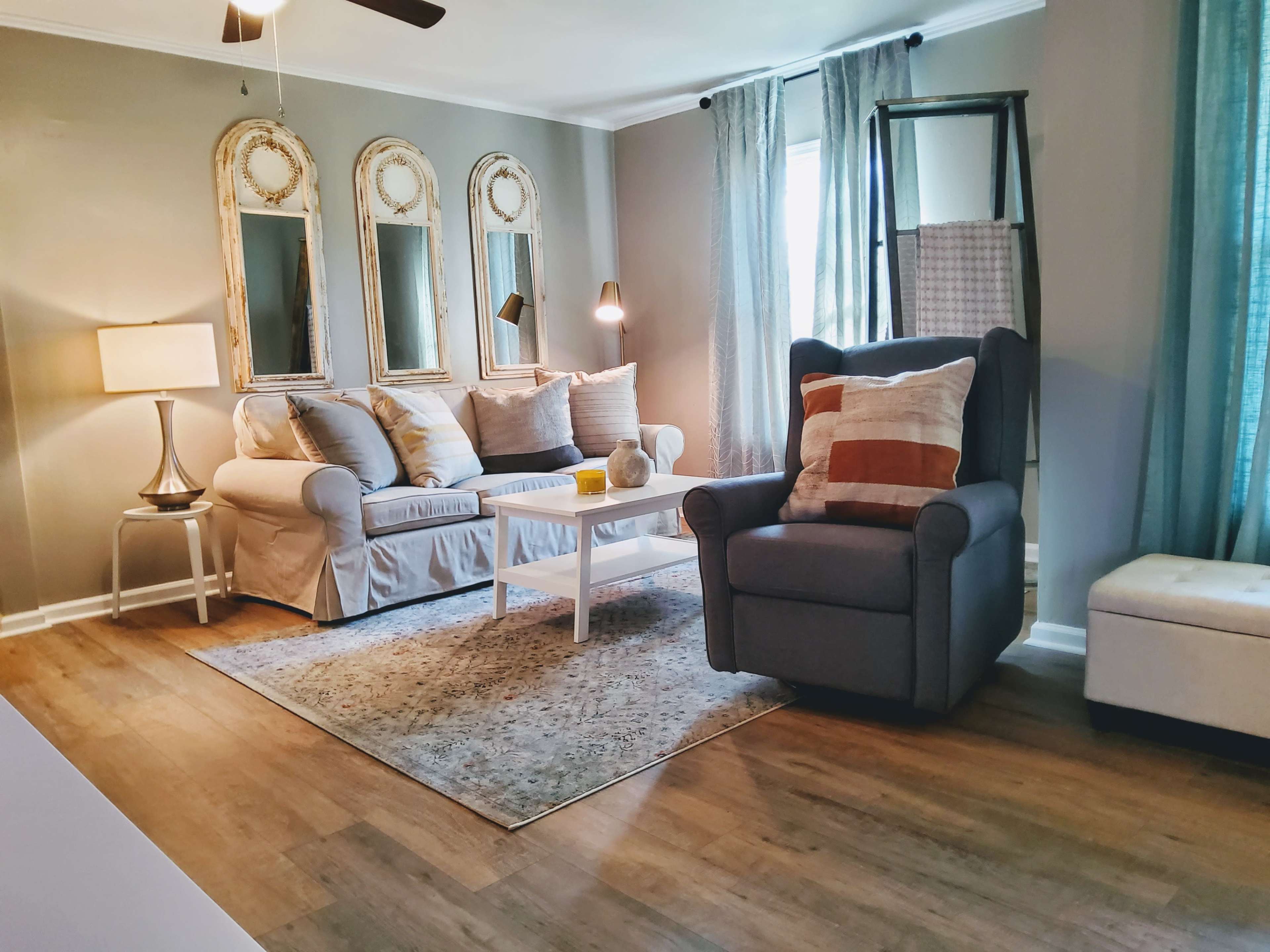 A cozy living room with a white couch, a gray armchair, a small coffee table, and decorative mirrors on the wall.