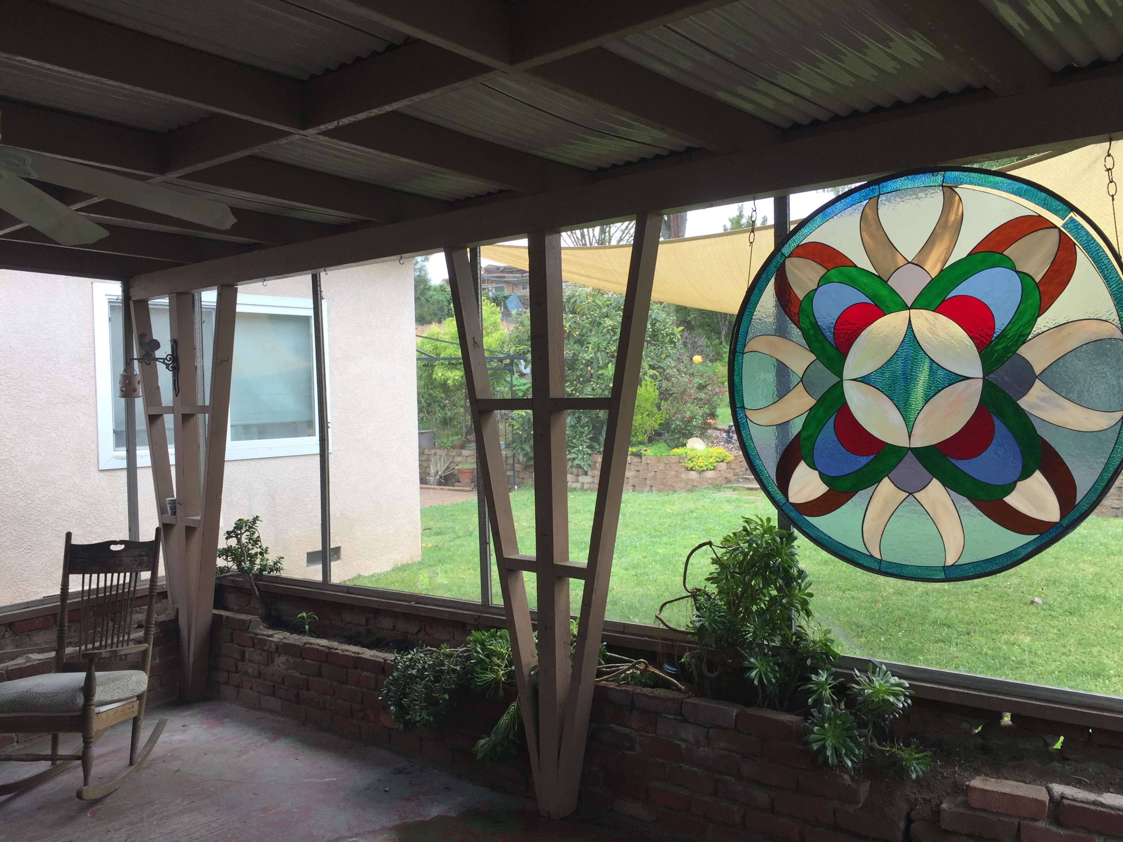 A covered porch featuring a rocking chair, a glass wall, and a large stained glass window with a geometric design.