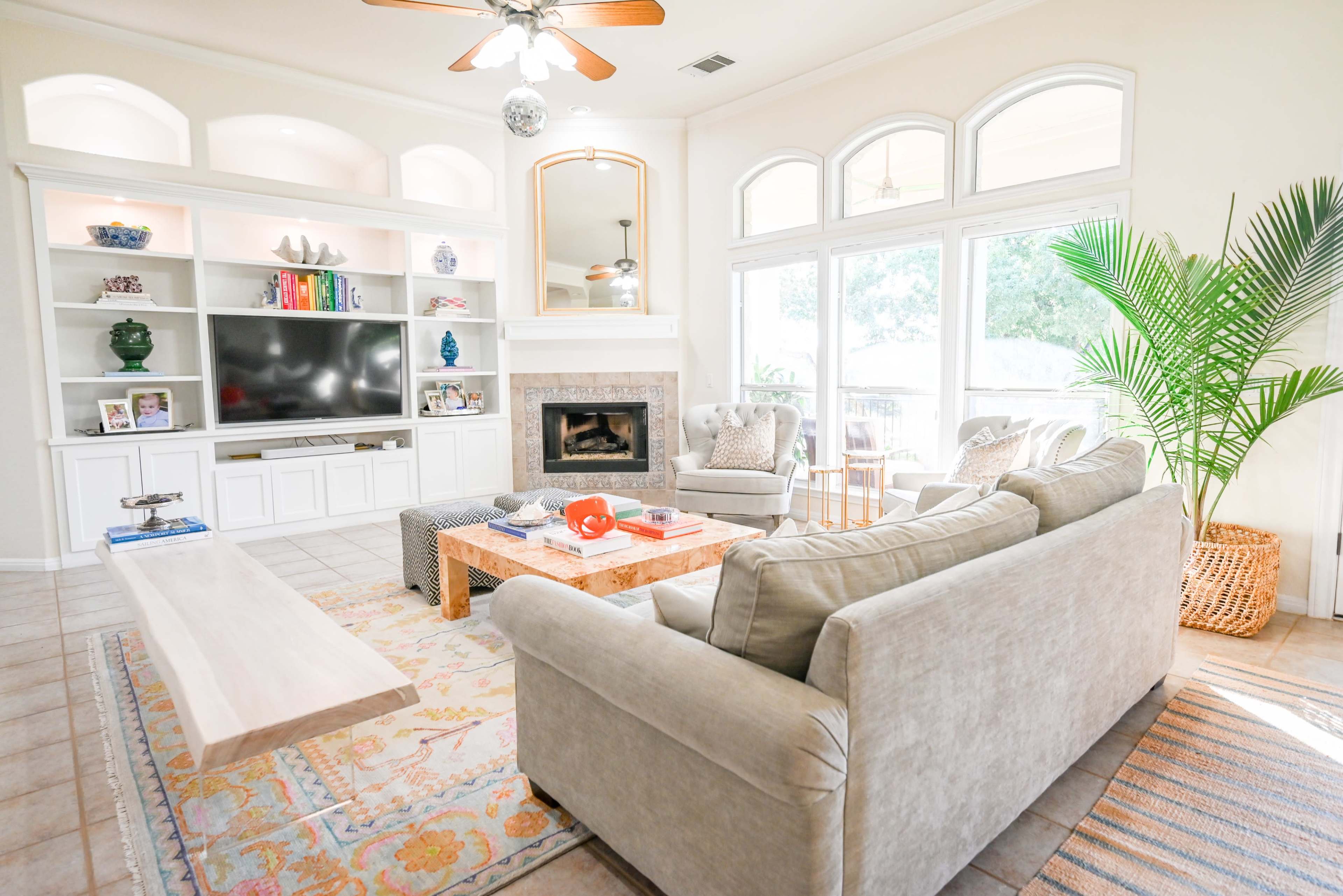 The living room features a white entertainment center, a light-colored sofa, a coffee table, and large windows providing ample natural light.